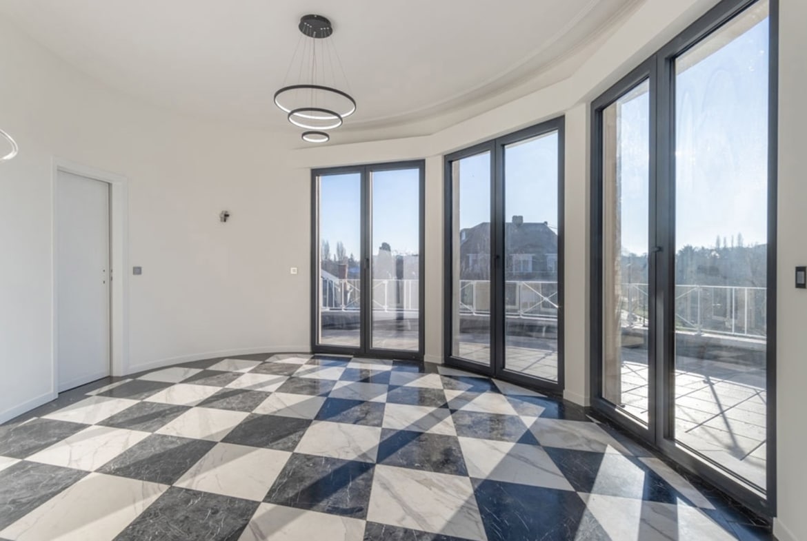 Bright empty living area with curved glass doors and a black-and-white checkerboard marble floor.