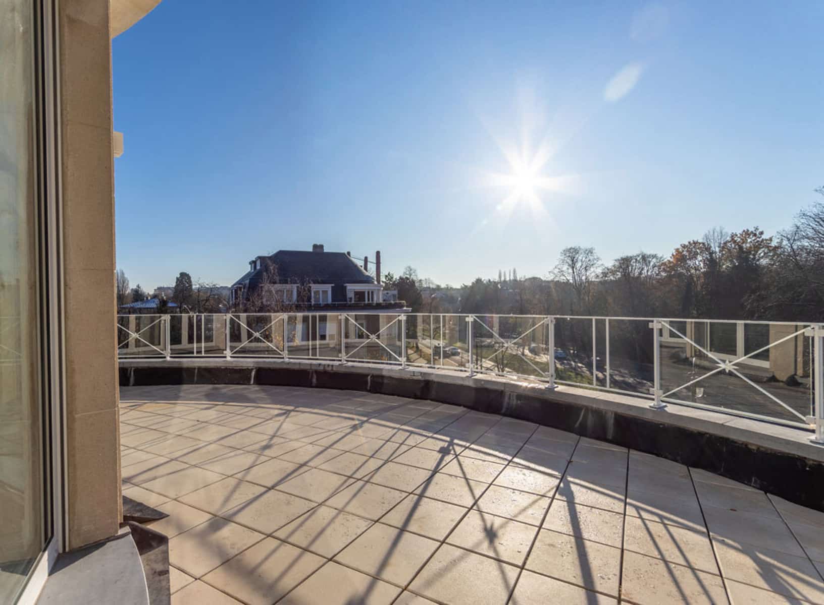 whise photo 7 Sunlit rooftop terrace with tiled floor and white crisscross railing overlooking a suburban neighborhood.