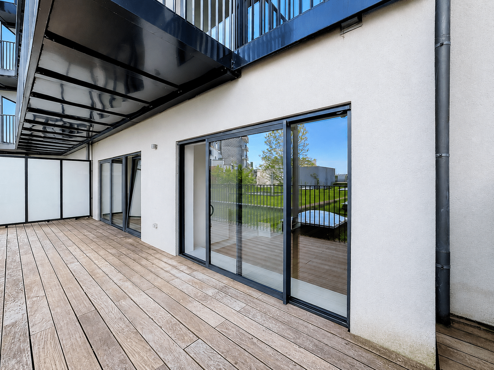 Terrasse en Bois avec Baies Vitrées – You Real Estate Agency Terrasse en bois d’un appartement moderne avec baies vitrées et balcon couvert.