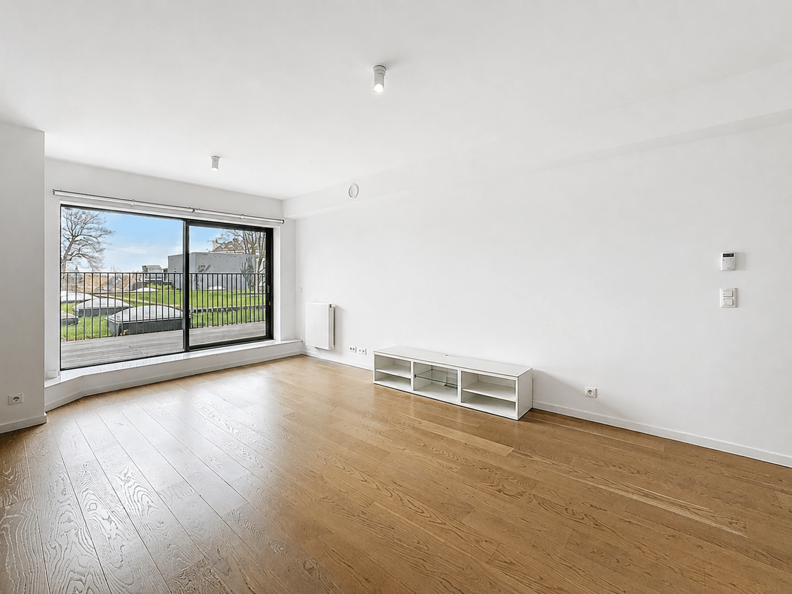 whise photo 3 Bright empty living room with a large sliding glass door to a balcony, light wooden floor and white walls.