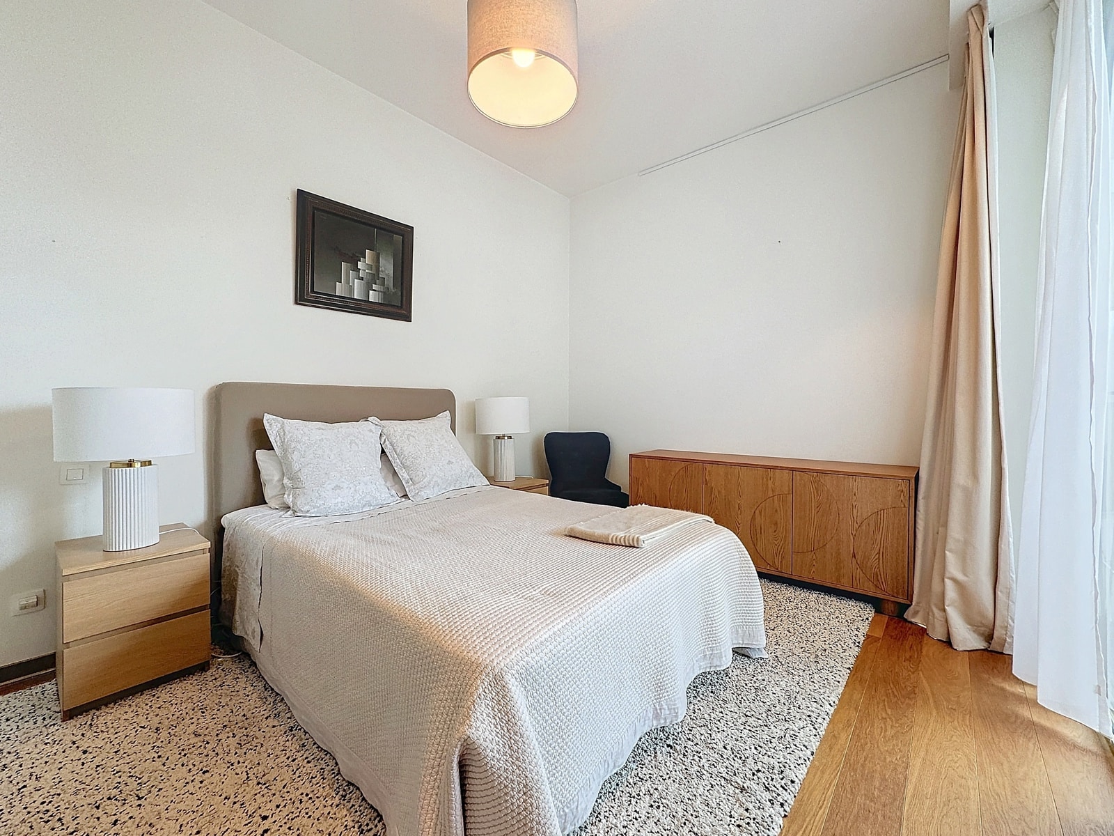 Chambre Lumineuse avec Lit Double – You Real Estate Agency Chambre lumineuse d’appartement avec lit double, parquet, rideaux et décoration minimaliste.