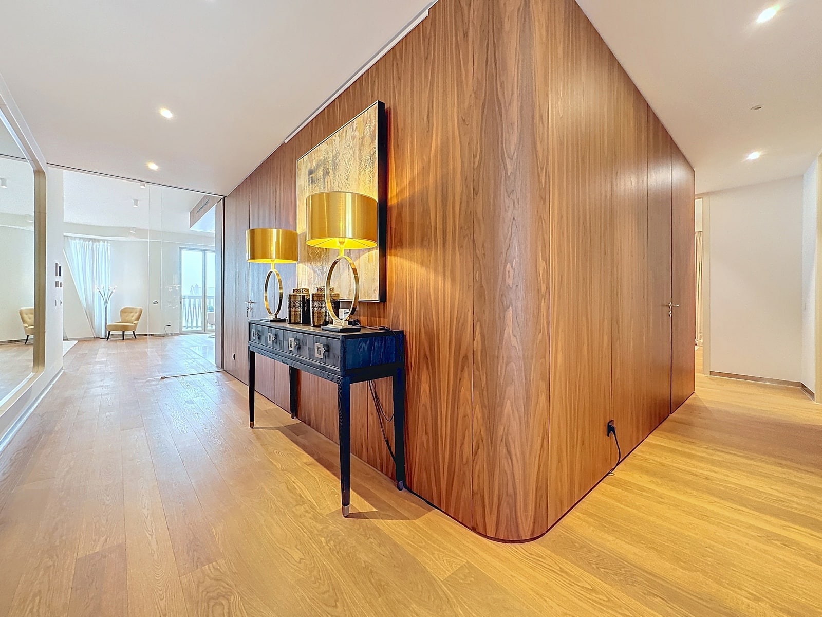 whise photo 7 Modern foyer with a curved walnut wall, a black console table, two gold lamps, and abstract wall art above.