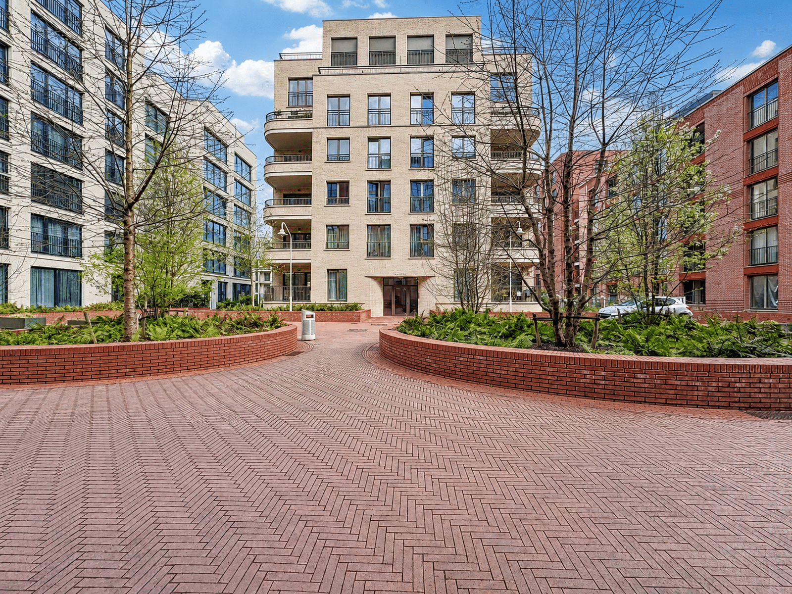 Résidence Moderne avec Cour Paysagée – You Real Estate Agency Cour intérieure paysagée d’une résidence d’appartements modernes avec balcons et entrée.
