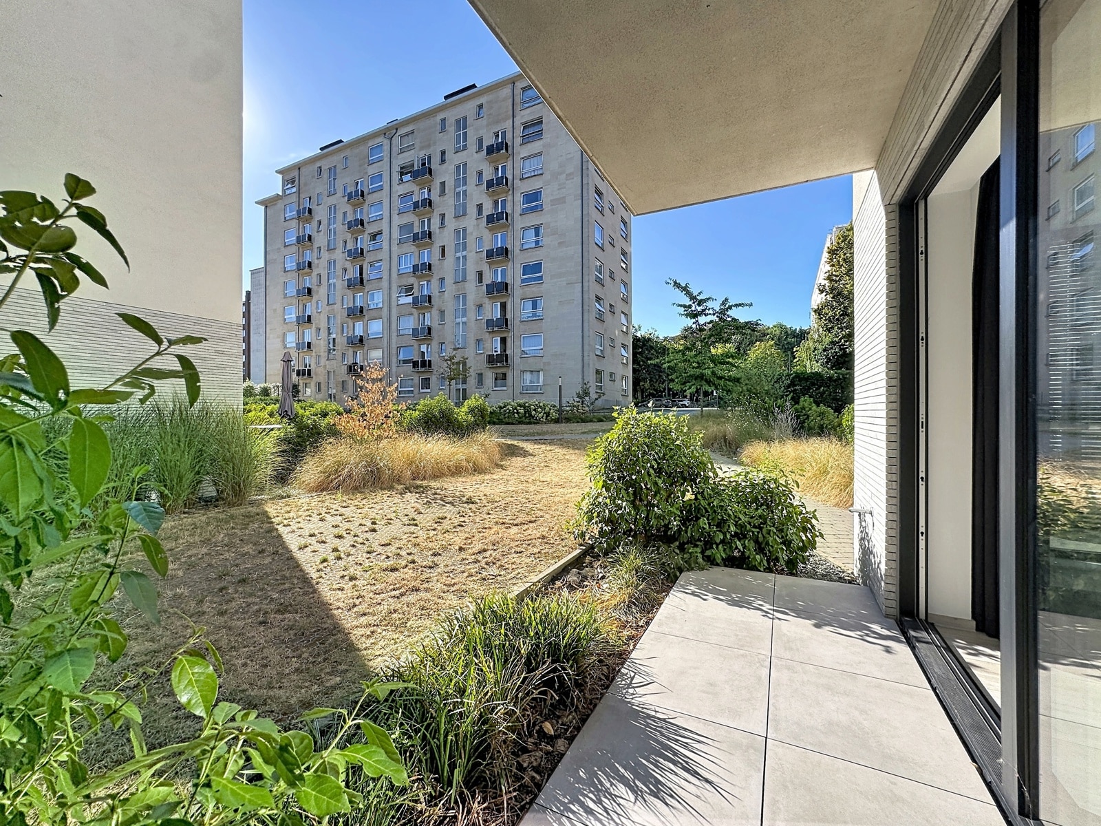 Apartment Terrace with Garden – You Real Estate Agency Modern apartment terrace overlooking a landscaped garden and a contemporary residential complex.