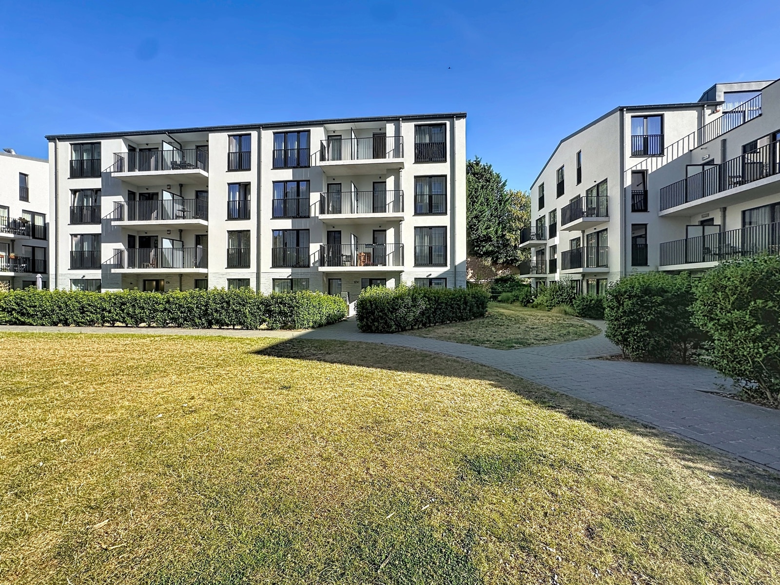 Modern Home with Garden – You Real Estate Agency A modern residential complex featuring apartments, terraces, and a sunny landscaped garden.