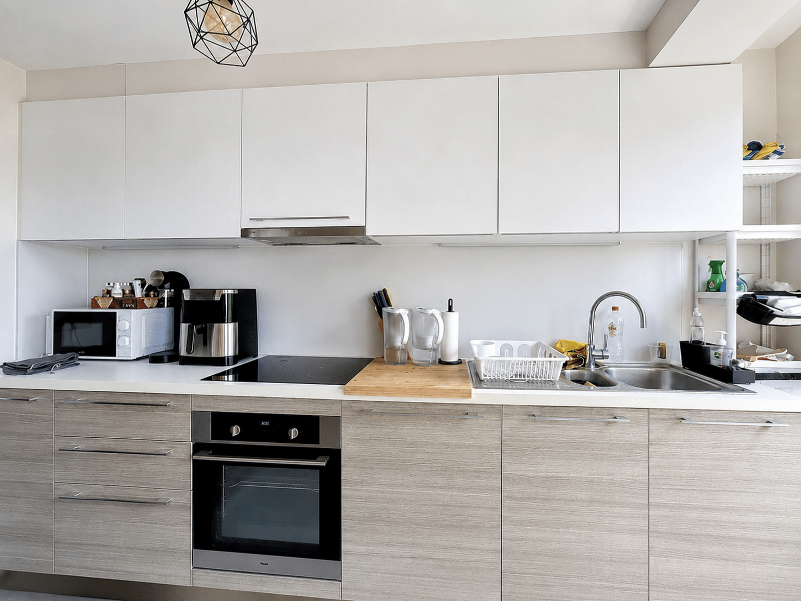 whise photo 3 Modern kitchen with white upper cabinets, light wood lower cabinets, built-in oven and stove, microwave, and a coffee station on the counter.