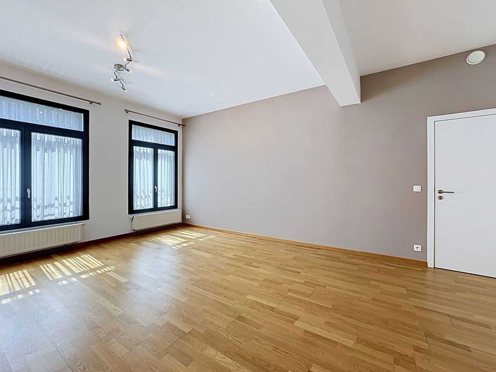 Bright living room with light parquet - You Real Estate Agency Bright living room in an unfurnished apartment with light-colored hardwood floors, large windows, and taupe walls.