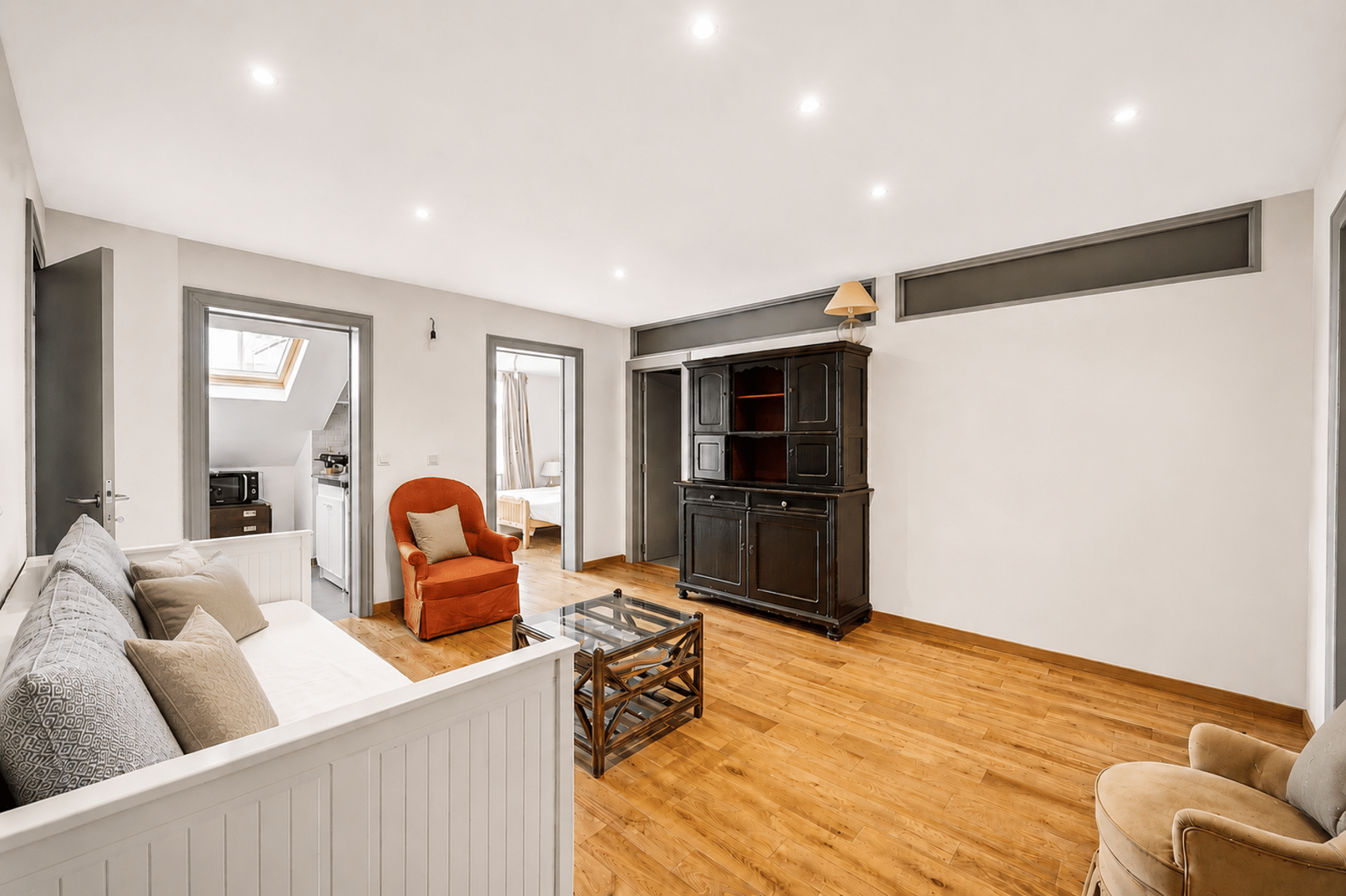 Lichte woonkamer met parketvloer - You Real Estate Agency Lichte woonkamer met parketvloer, witte bank en open keuken in een modern appartement.
