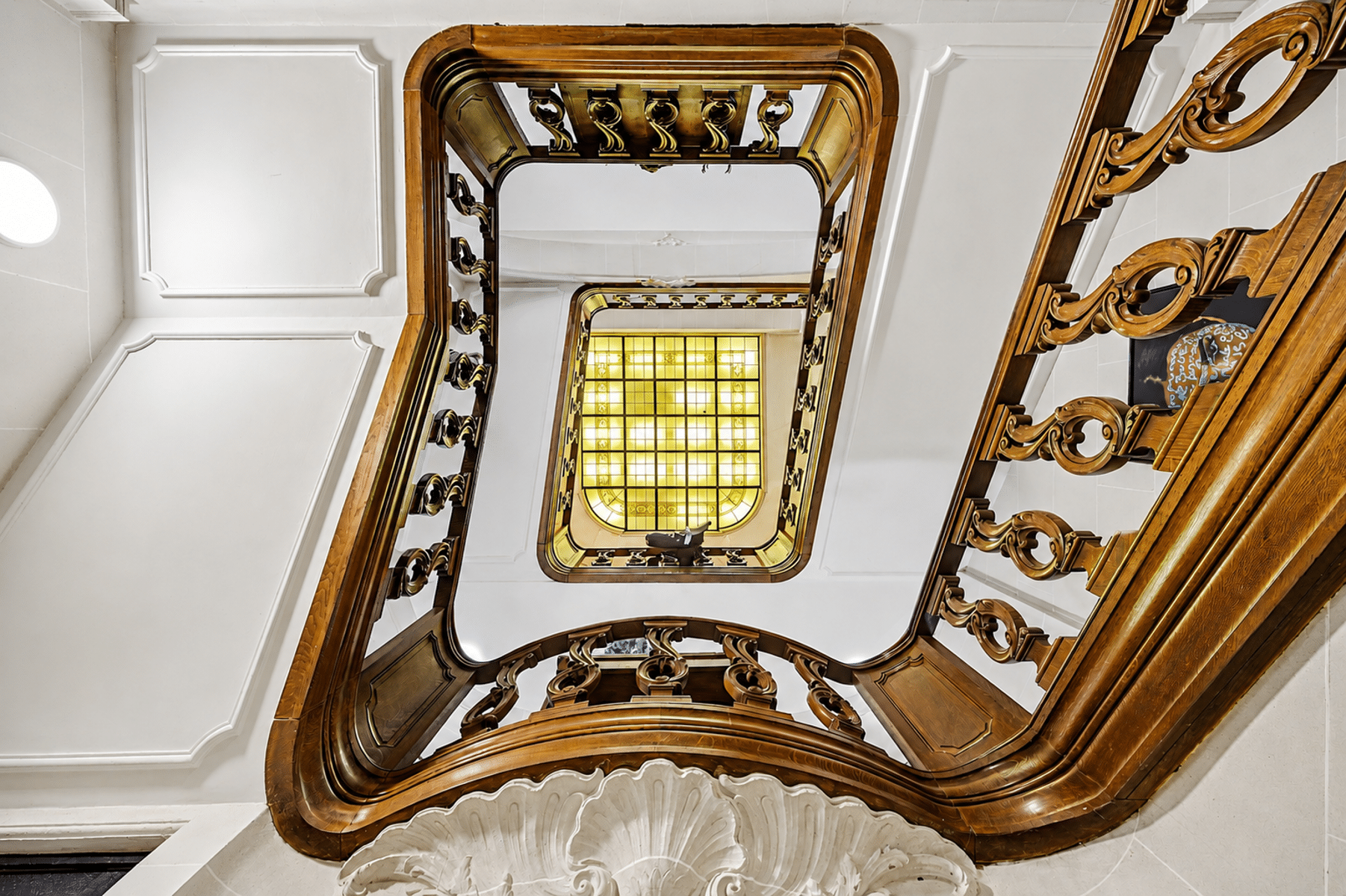 Houten trap met lichtkoepel – You Real Estate Agency Een majestueuze binnentrap van bewerkt hout met een lichtkoepel in een karakteristiek huis.