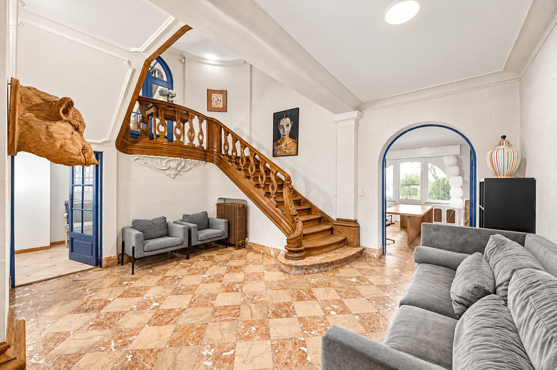 Ruime woonkamer met houten trap – You Real Estate Agency Ruime woonkamer van een huis met een houten trap en een marmeren vloer.