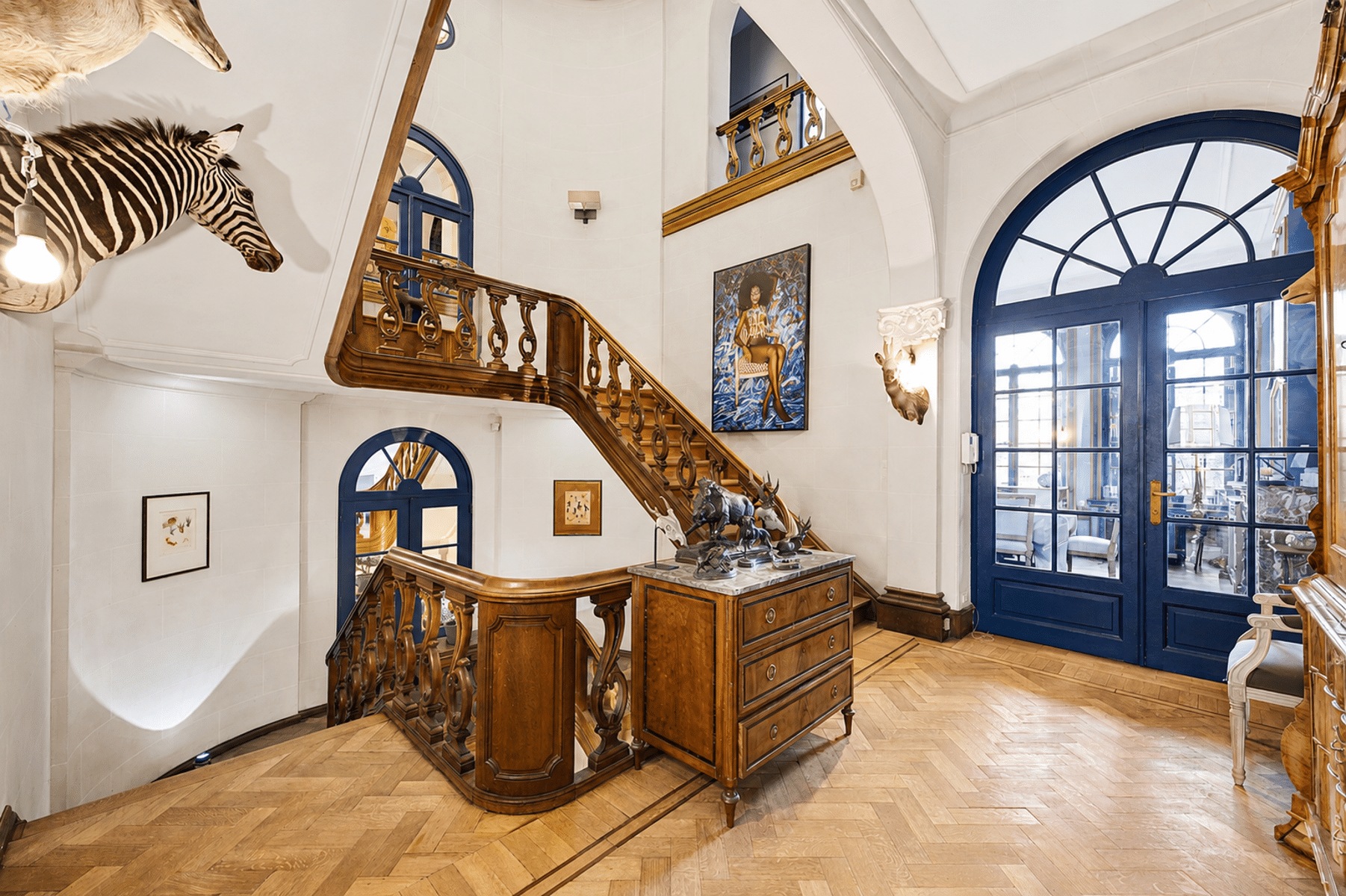 Eclectische hal met trap – You Real Estate Agency Entreehal van een huis met een houten trap, parketvloer en blauwe boogdeuren.