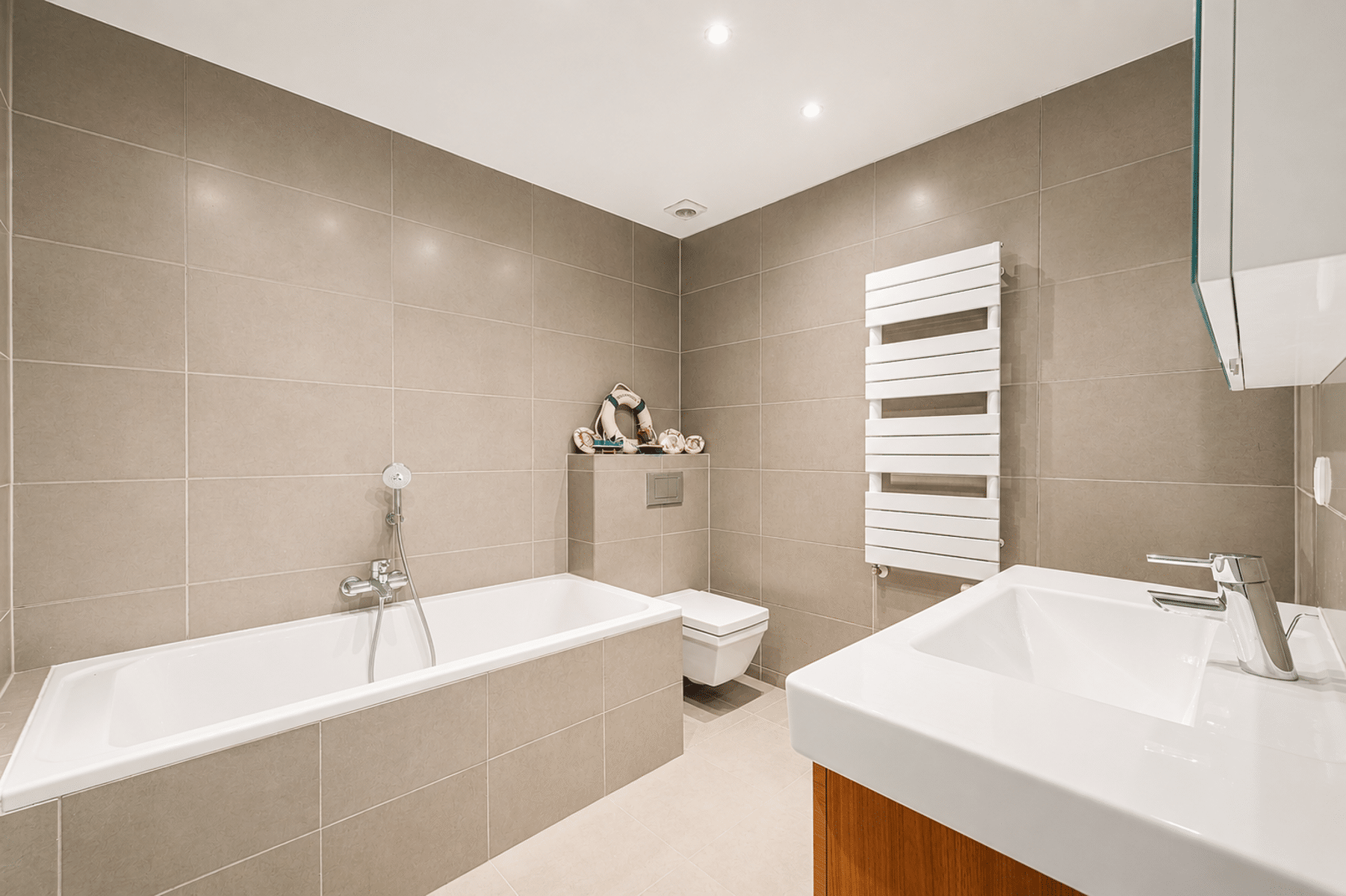 Moderne badkamer – You Real Estate Agency Moderne badkamer met bad, wastafel en toilet in een eigentijds appartement.