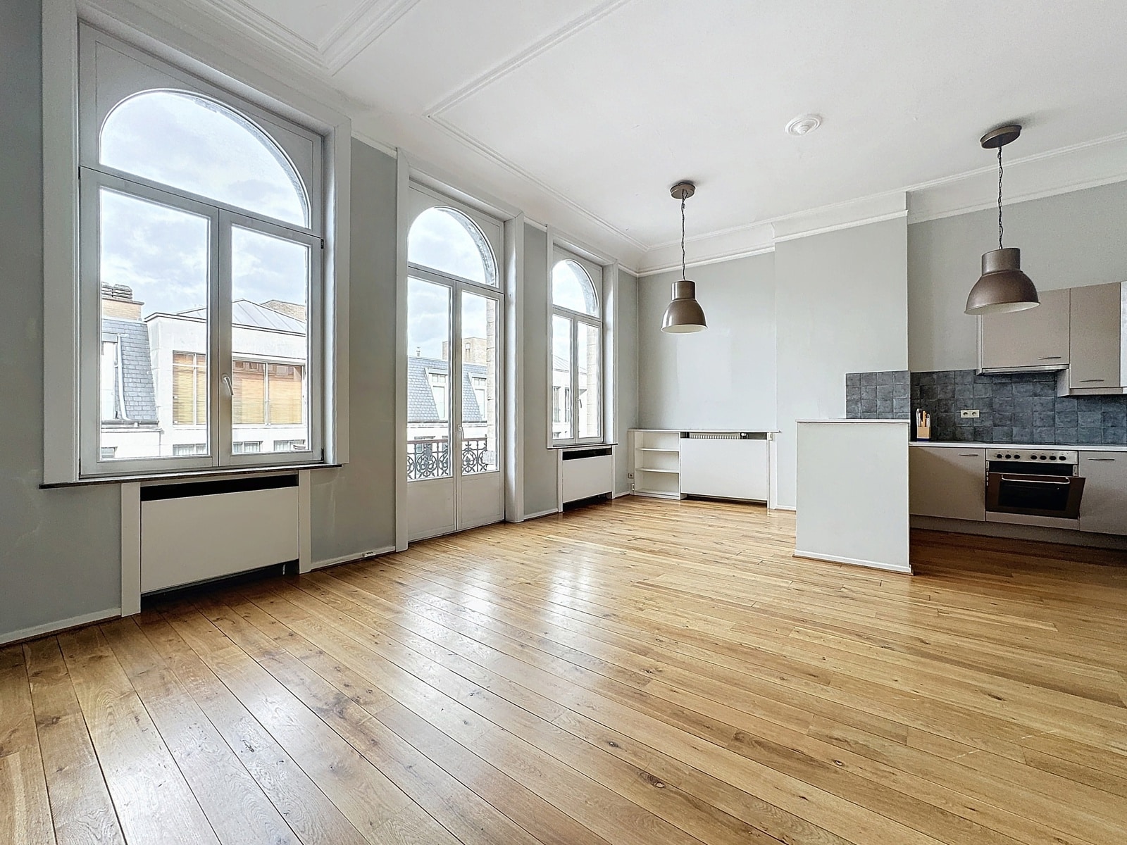 Lichte woonkamer met open keuken - You Real Estate Agency Licht appartement met woonkamer, open keuken, parketvloer en grote boogramen.