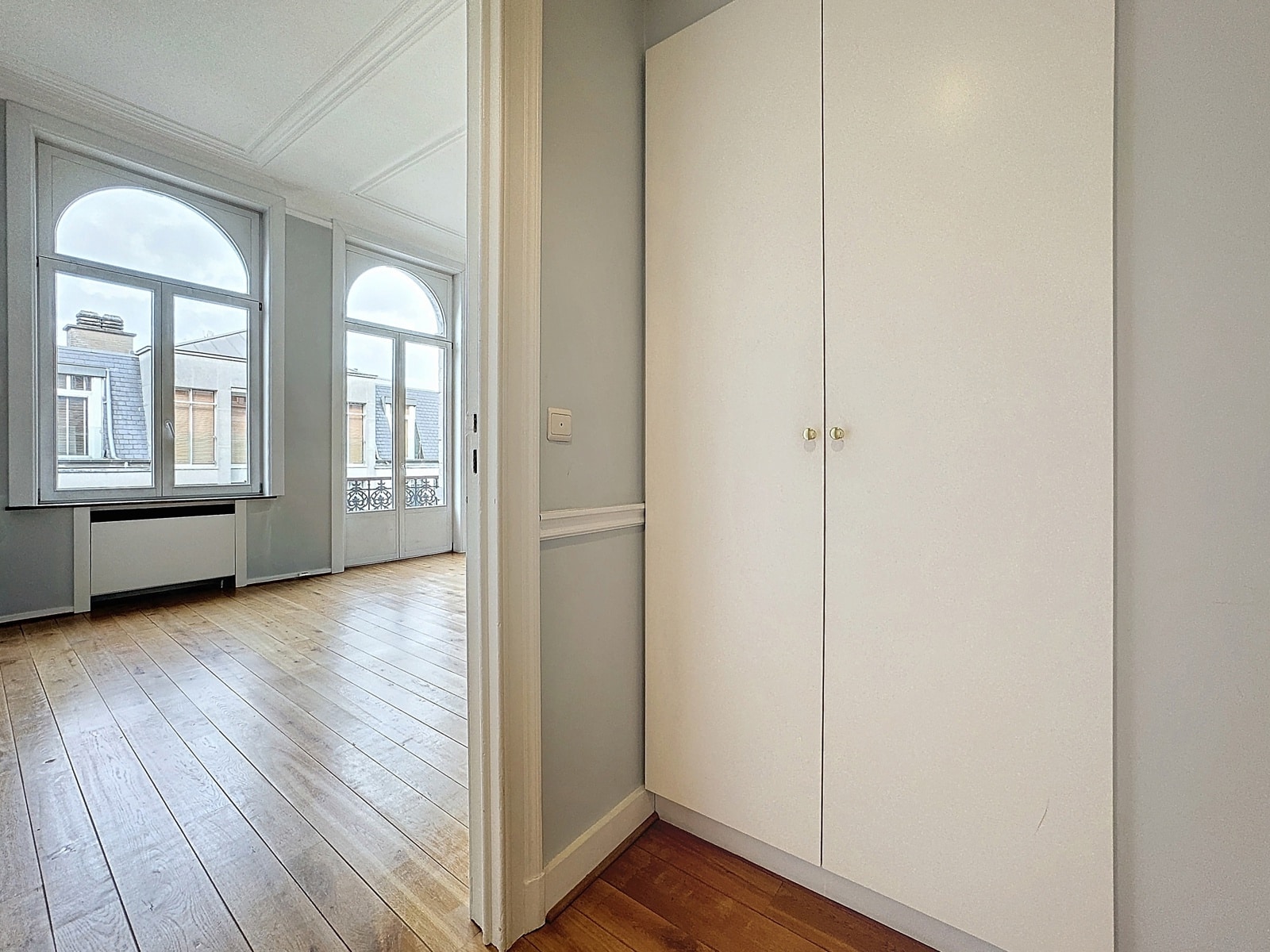 foto 6 Lichte, lege kamer met hoge boogramen en een lichte houten vloer; aan de rechterkant een witte inbouwkast.