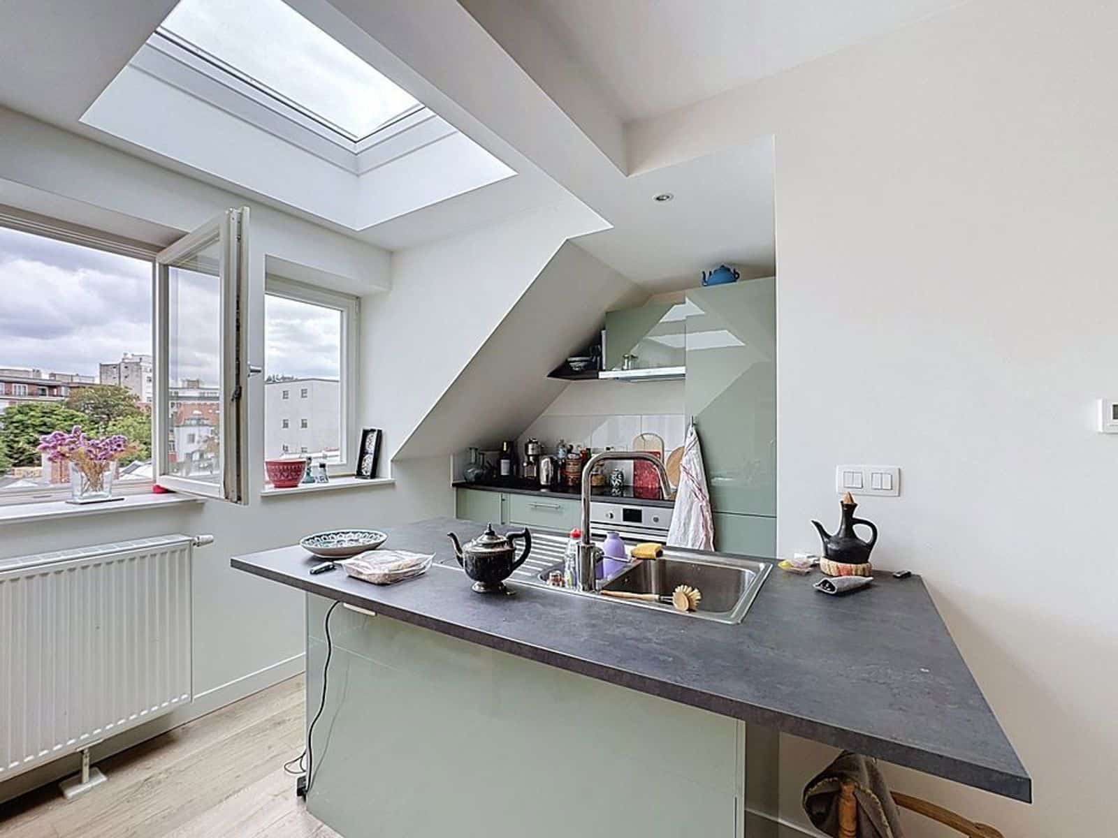 whise photo 3 Bright kitchen with a sloped ceiling, skylight and an open window overlooking the city; island countertop with sink and dishes nearby.