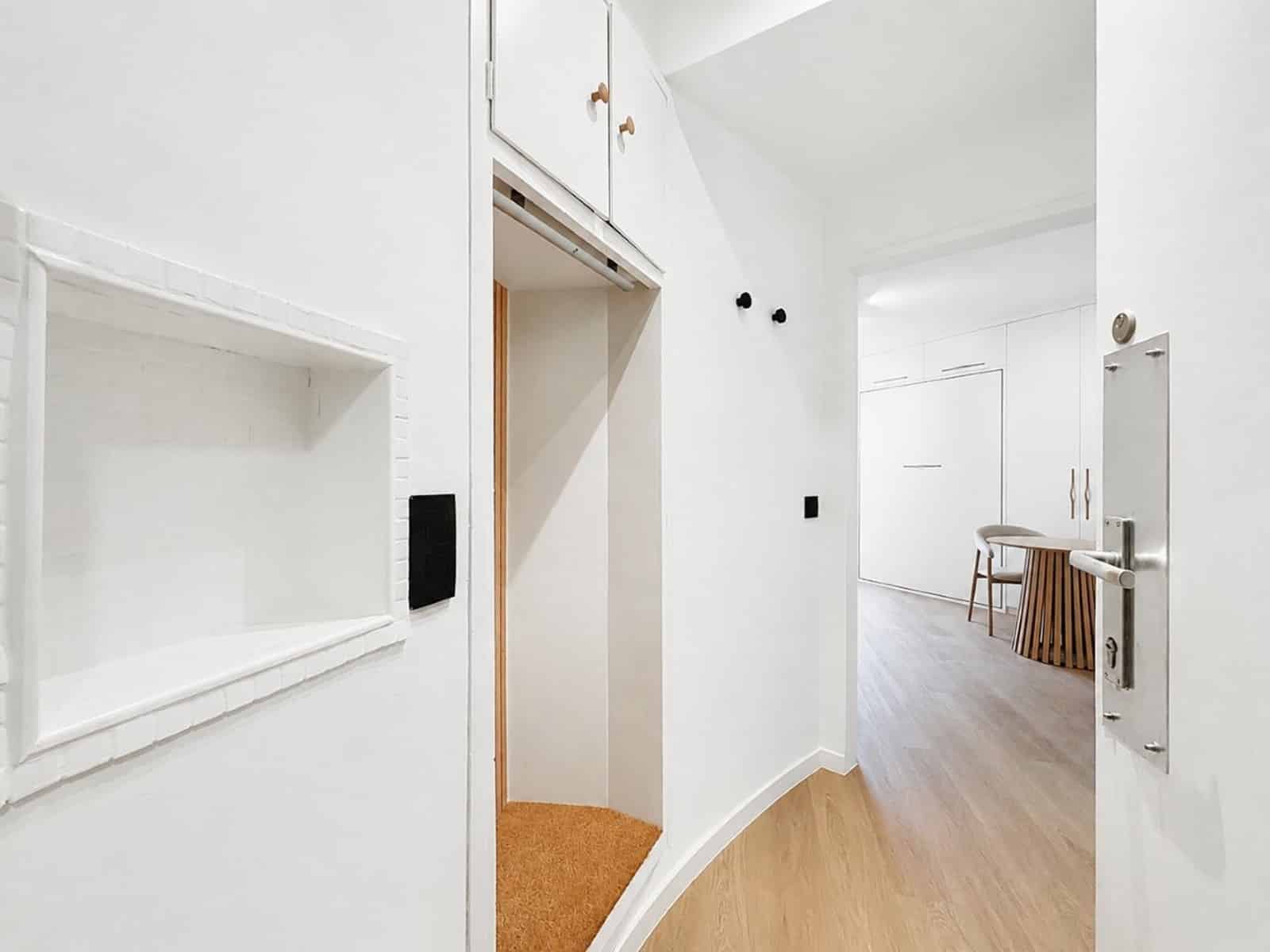 whise photo 4 Bright white hallway with an open elevator alcove on the left and a curved wood floor leading to a room with a round table.