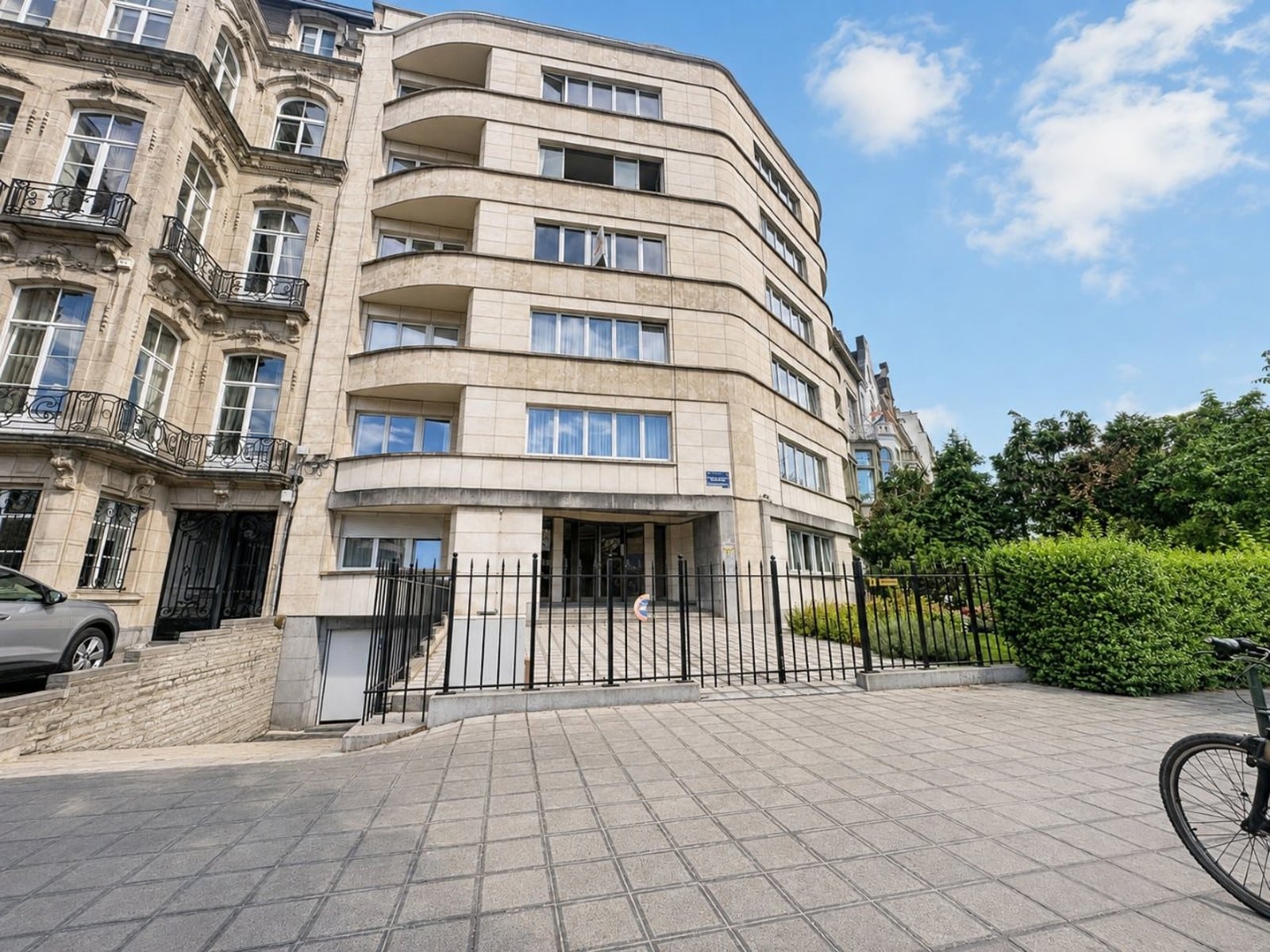 whise photo 12 Curved beige apartment building with balconies and a gated entrance on a paved street, blue sky overhead.