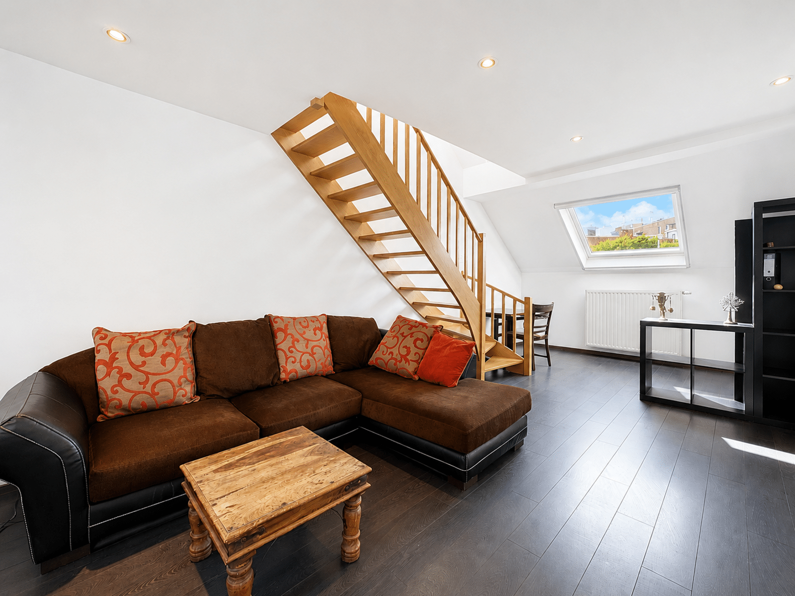 Salon Mansardé Lumineux Avec Escalier – You Real Estate Agency Salon d’appartement mansardé lumineux avec escalier en bois et canapé d’angle.