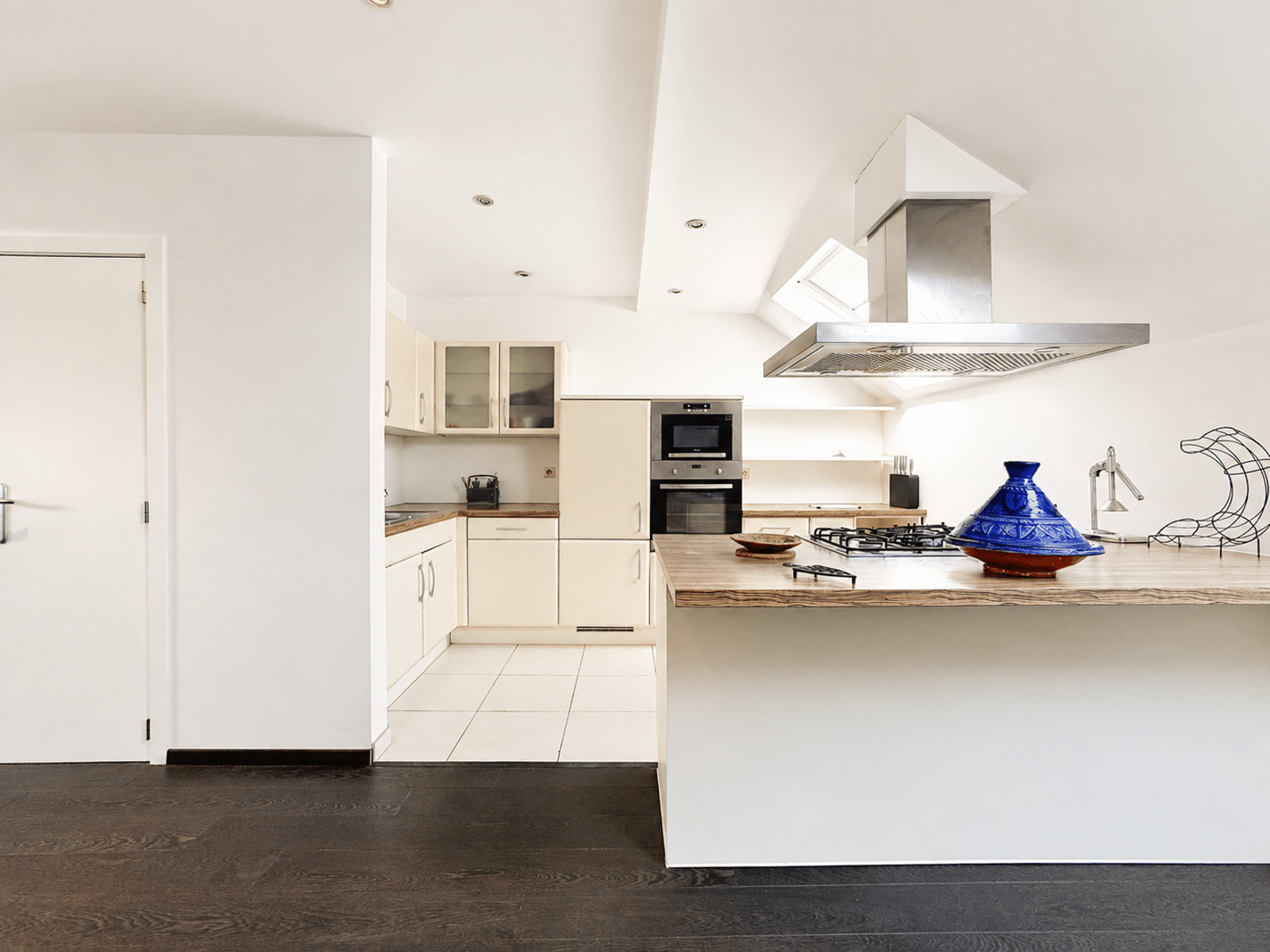 whise photo 3 Bright modern kitchen with a large island, built-in oven, and stainless steel range hood; blue ceramic tagine on the counter.