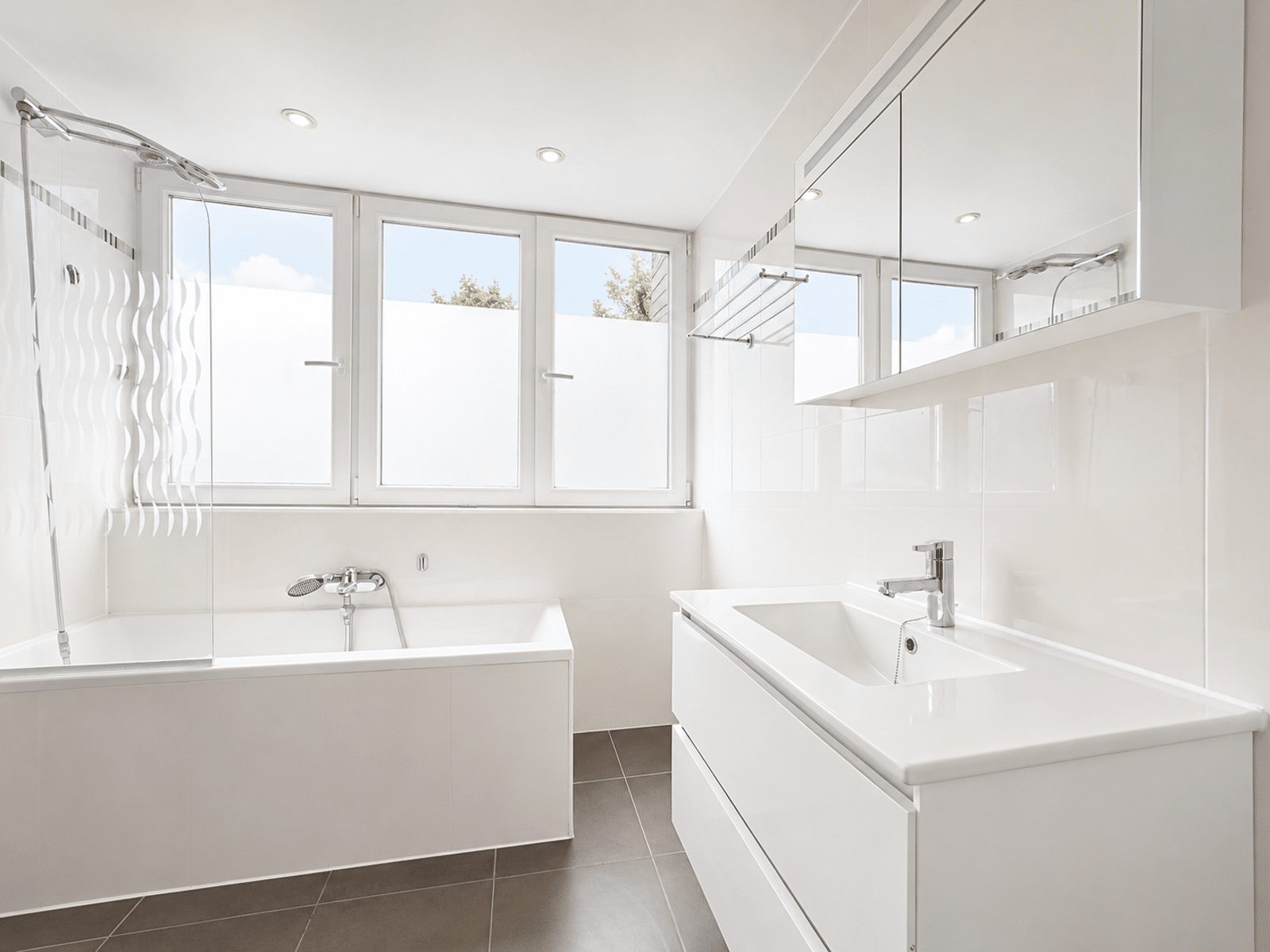 Salle de Bain Moderne et Lumineuse – You Real Estate Agency Salle de bain moderne d’appartement avec baignoire, douche vitrée et meuble vasque.