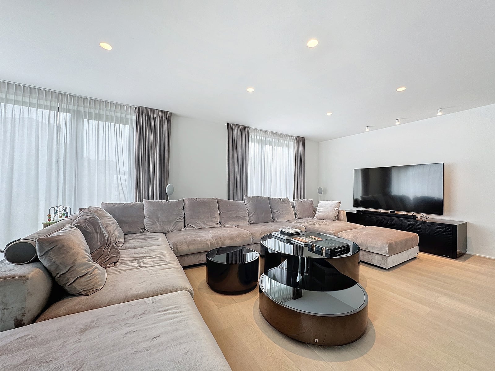whise photo 5 Spacious modern living room with a large light-gray sectional sofa, round glass coffee tables, and a flat-screen TV on a black console.