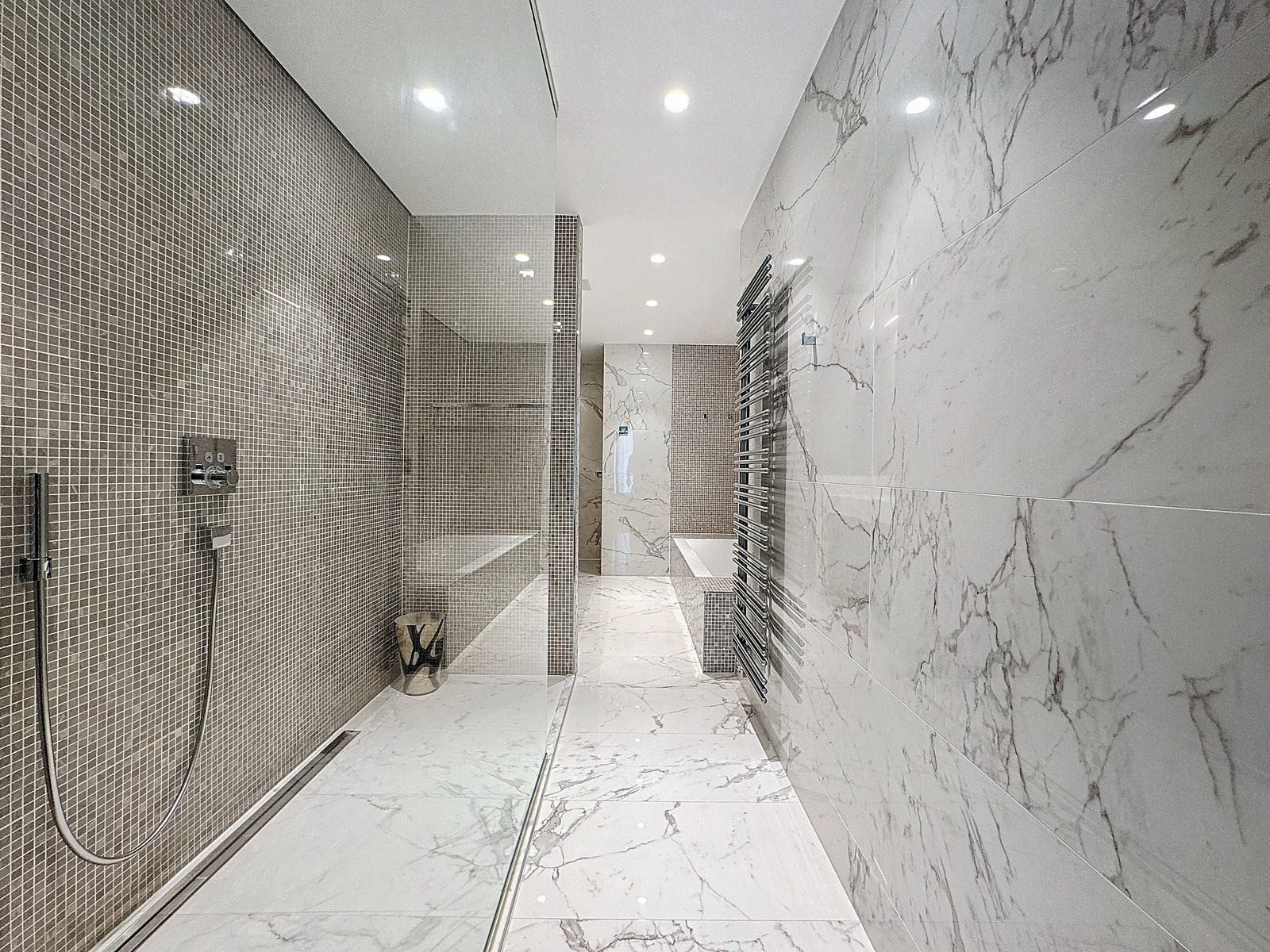 whise photo 17 Wide view of a modern marble bathroom featuring a glass-walled shower, mosaic tile walls, and a chrome towel radiator.