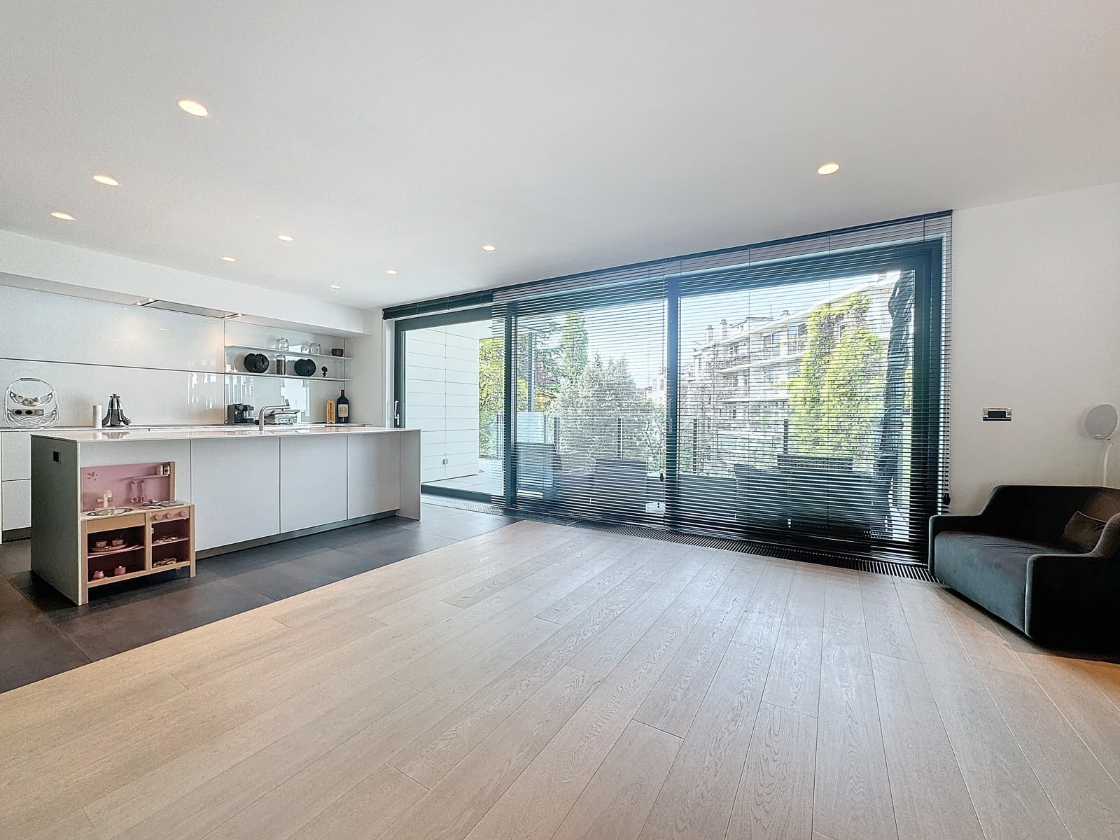 whise photo 10 Bright, modern open-plan kitchen and living room with white cabinets, a long island, open shelving, and large sliding glass doors with blinds.