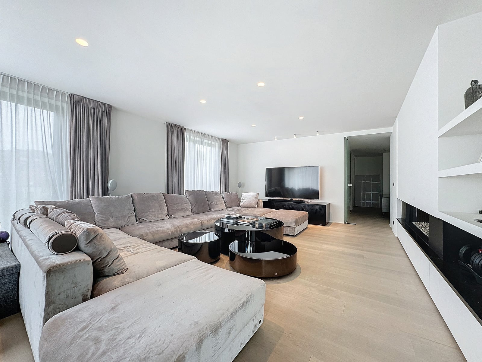whise photo 2 Spacious living room with a light gray sectional sofa, round glass coffee tables, and a wall-mounted TV in a bright, modern space.