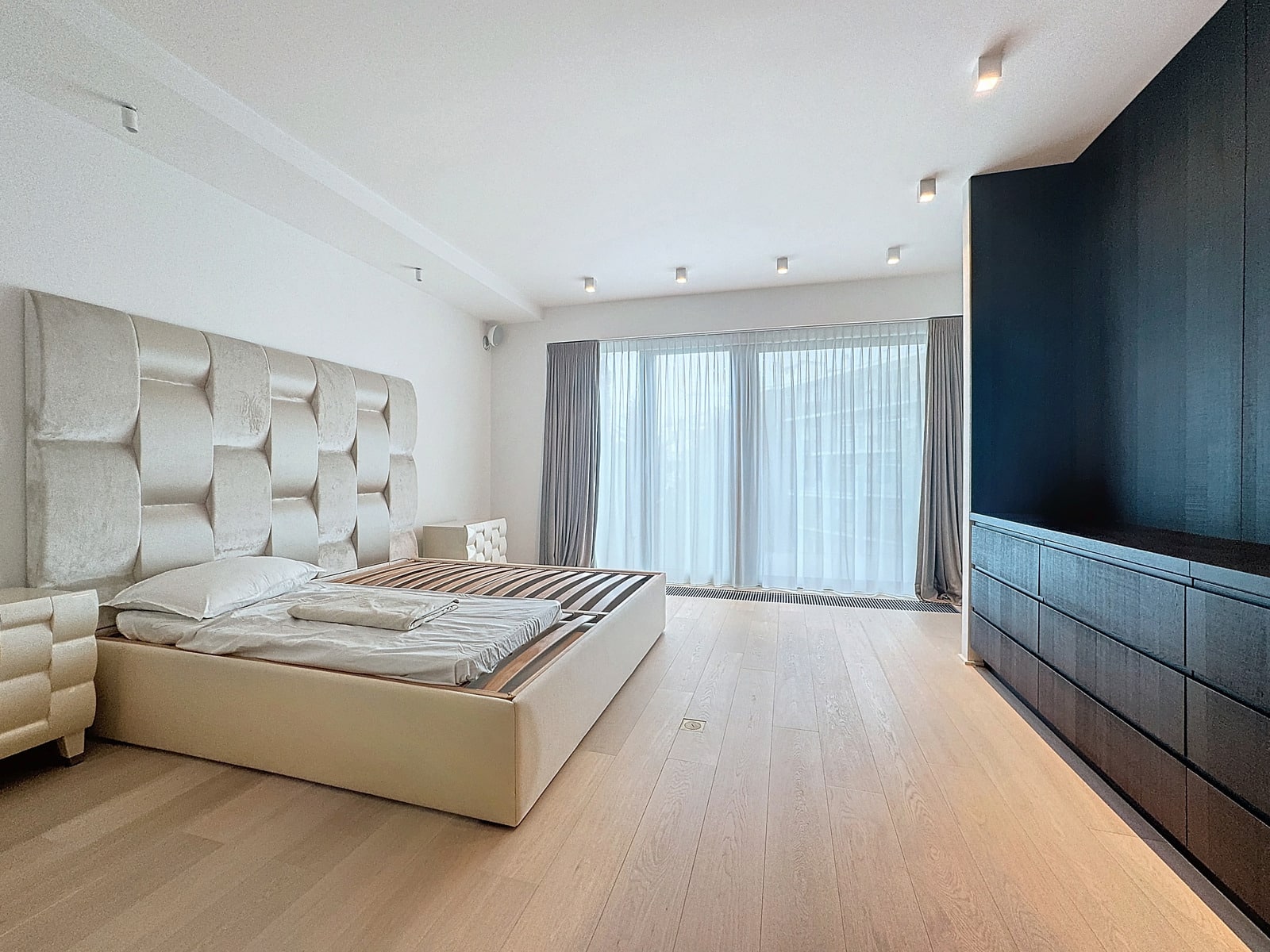 whise photo 16 Minimalist bedroom with a tall tufted beige headboard, platform bed, and large window with sheer curtains in soft natural light.