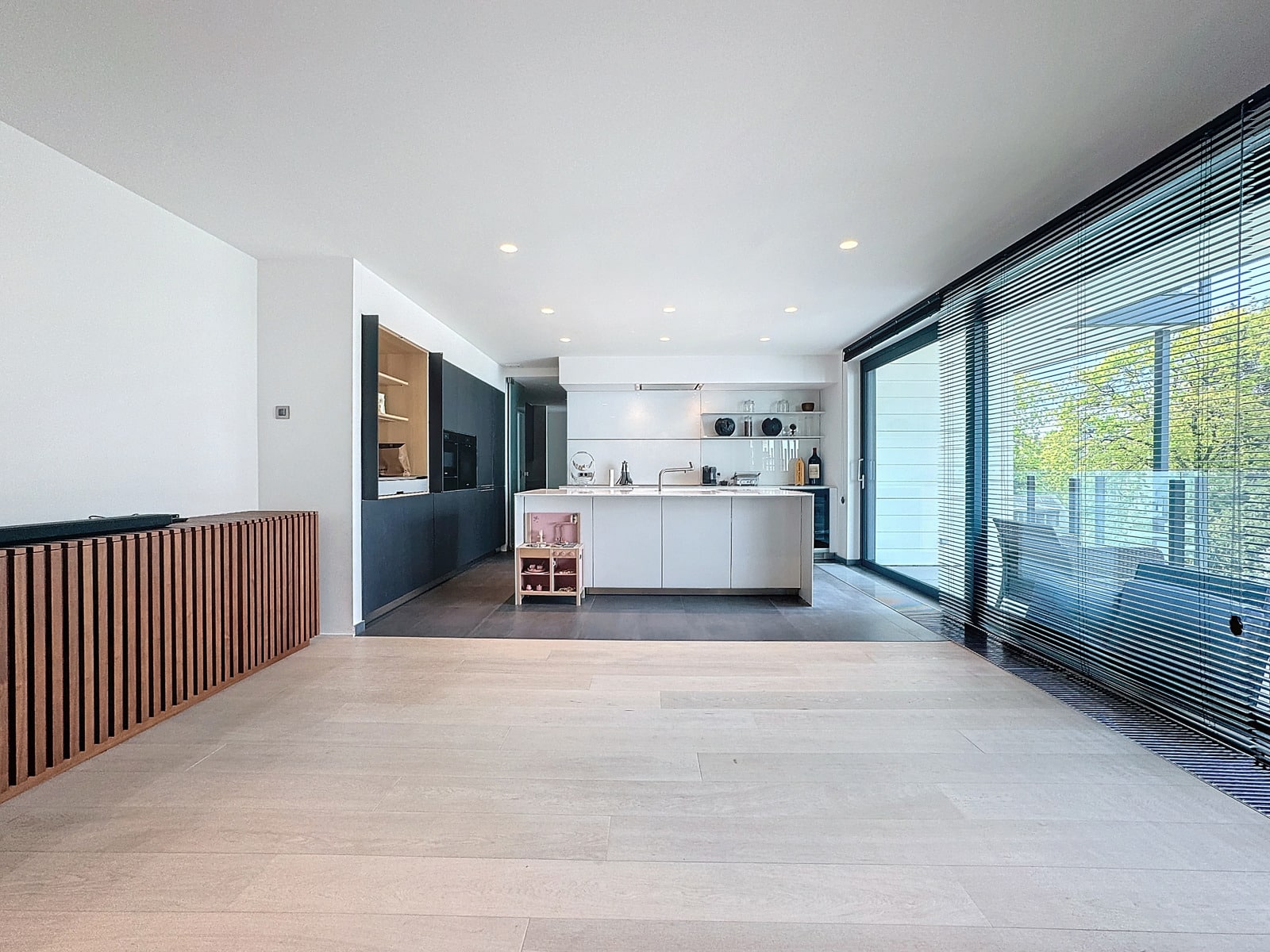 whise photo 6 Open-plan kitchen with a white island, dark cabinetry, and large glass doors with blinds bringing in natural light and a view outside.