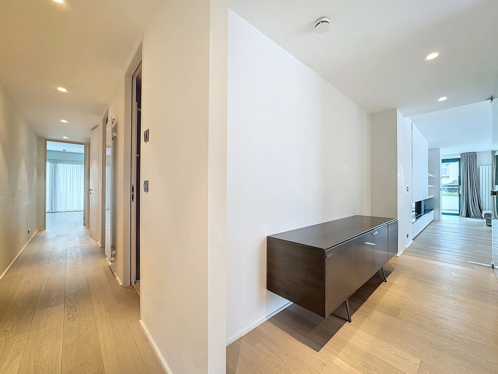 whise photo 15 Bright hallway in a modern apartment with light wood floors, white walls, and a dark glossy console against the right wall.