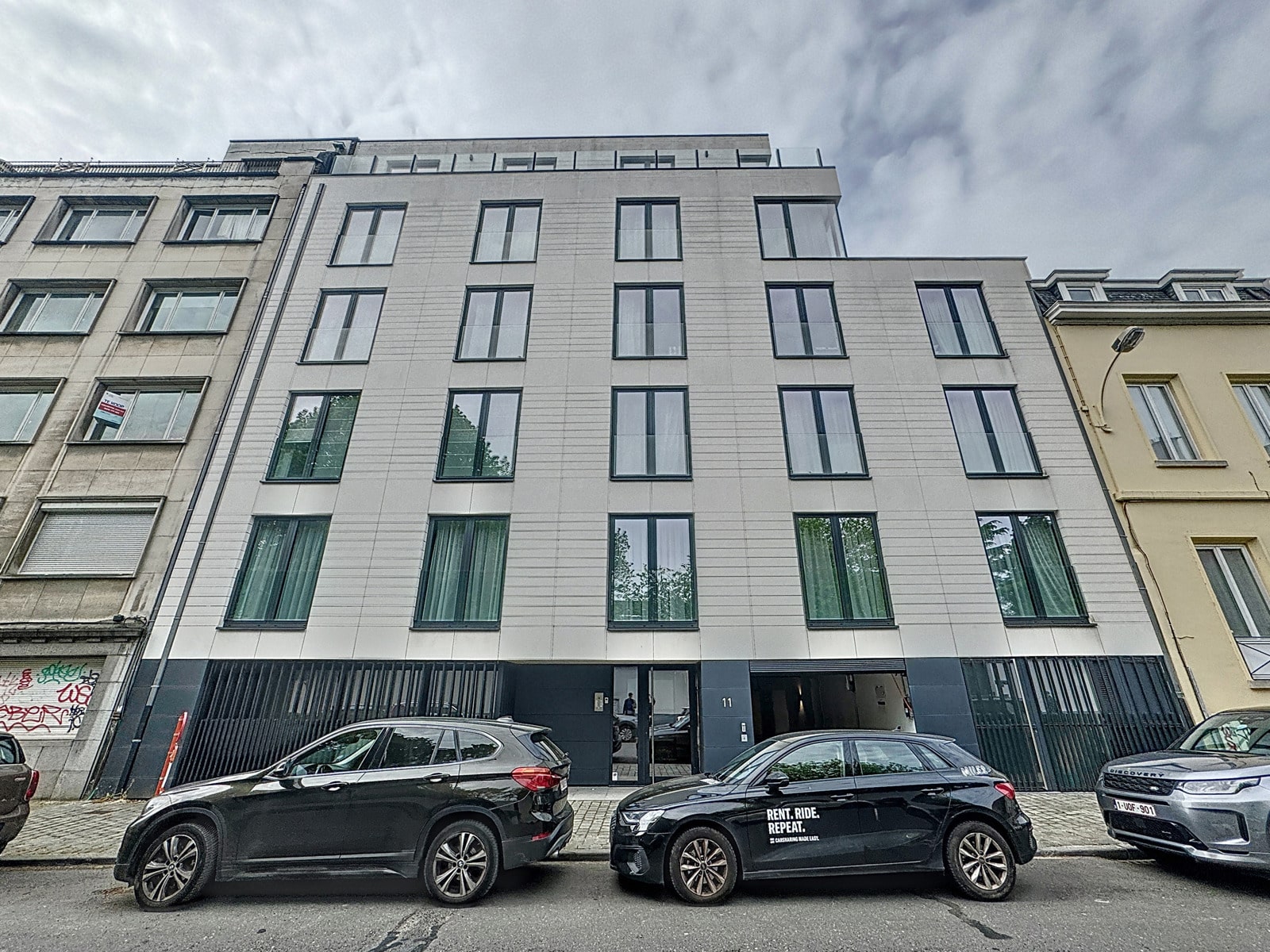 whise photo 21 Five-story modern building with large vertical windows, parked cars along the street in front of it.