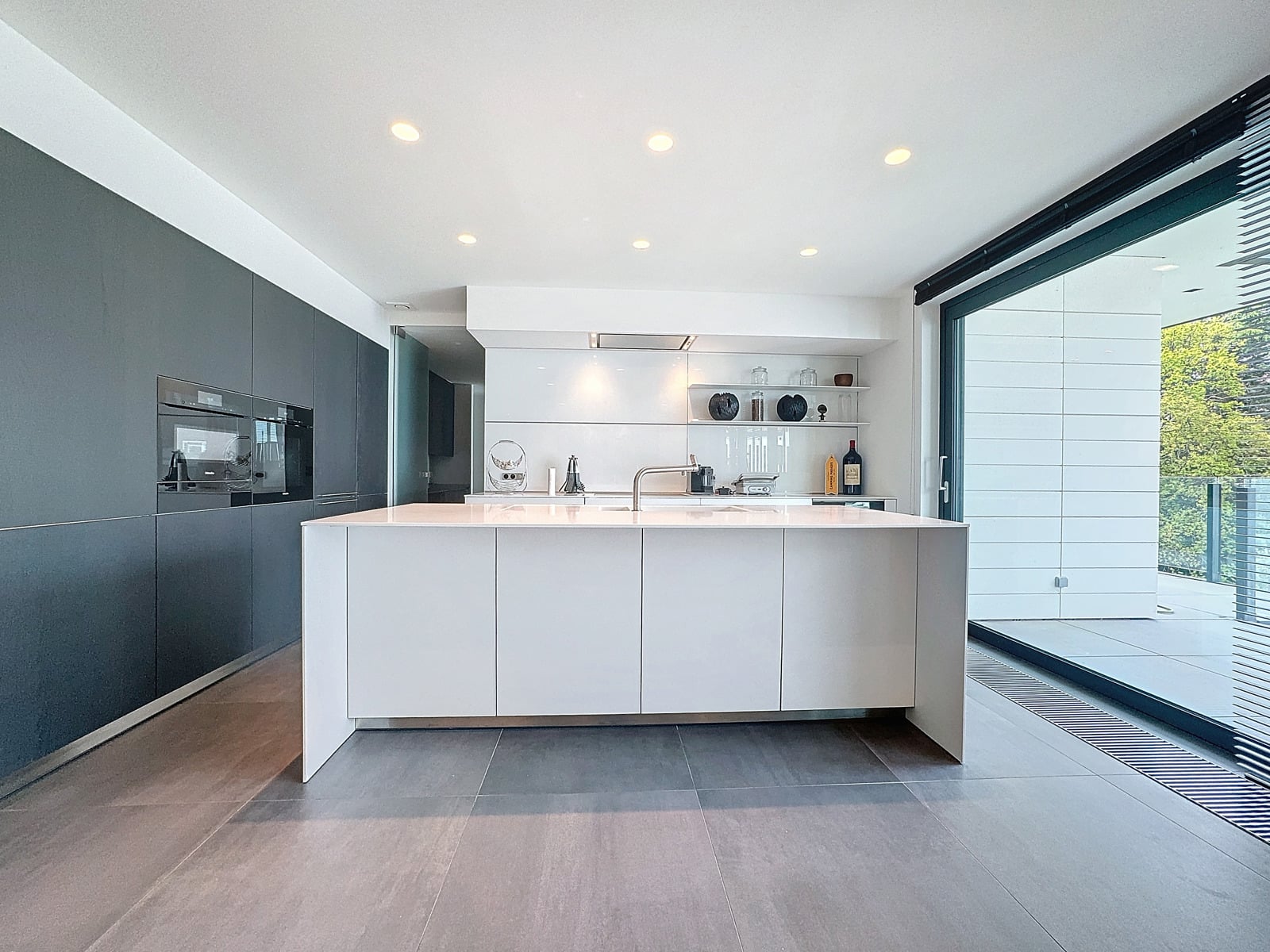 whise photo 7 Modern kitchen with white island, gray wall cabinets, and open shelves, opening to a sunny balcony via large glass doors.