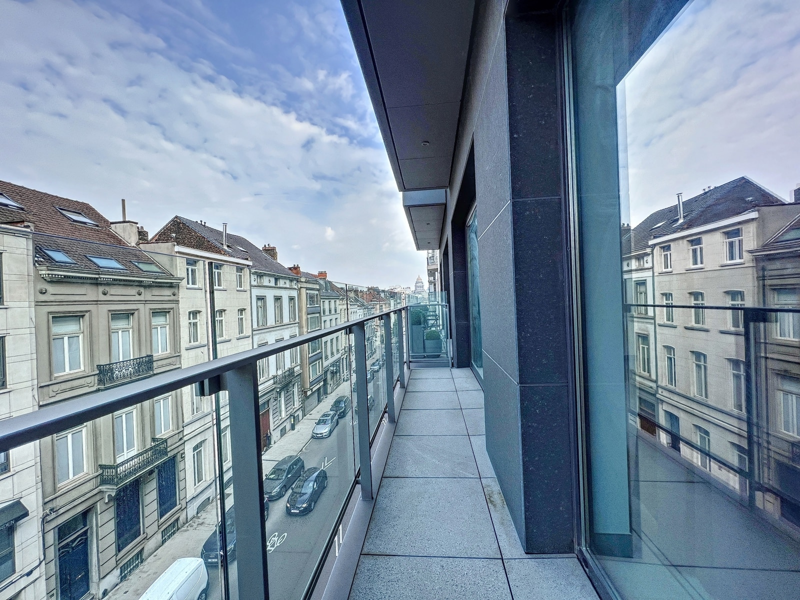 whise photo 8 Balcony view from a modern building looking down a street of classic European houses with parked cars and a blue sky ahead.
