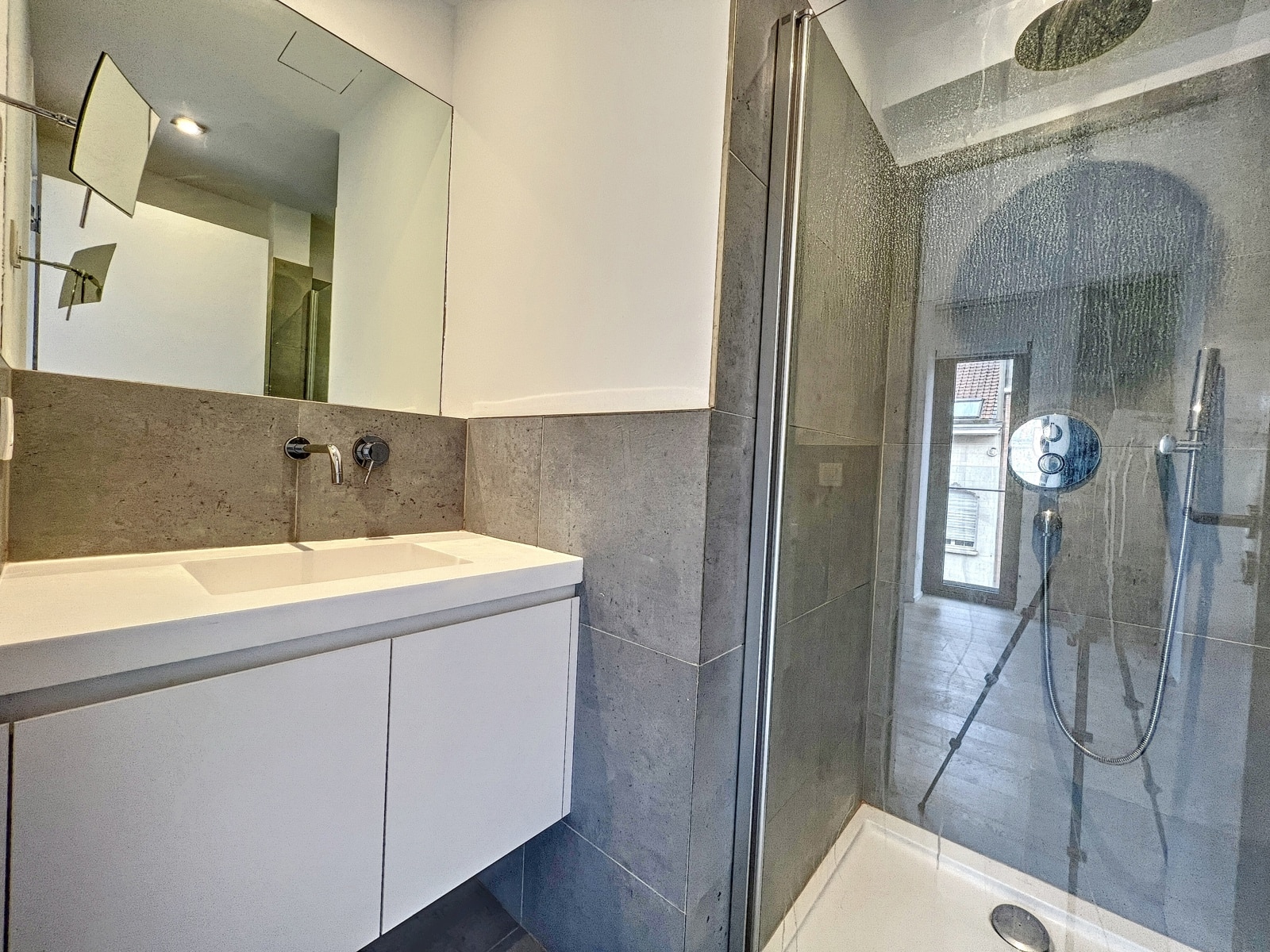 whise photo 13 White bathroom vanity with a wide sink, grey tiled walls, and a glass shower enclosure with a rainfall shower head on the ceiling and a handheld wand.