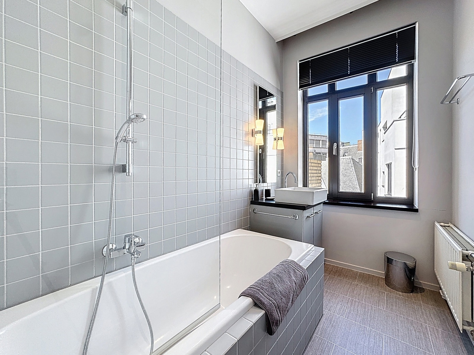 Salle de Bain Moderne avec Baignoire – You Real Estate Agency Salle de bain moderne d’appartement avec baignoire, douche vitrée et grande fenêtre.