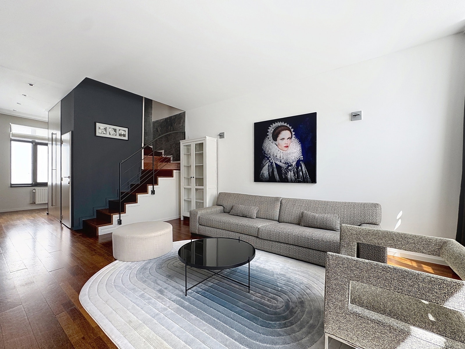 Salon Moderne avec Escalier – You Real Estate Agency Salon moderne avec escalier en bois, canapé gris et grand portrait mural.