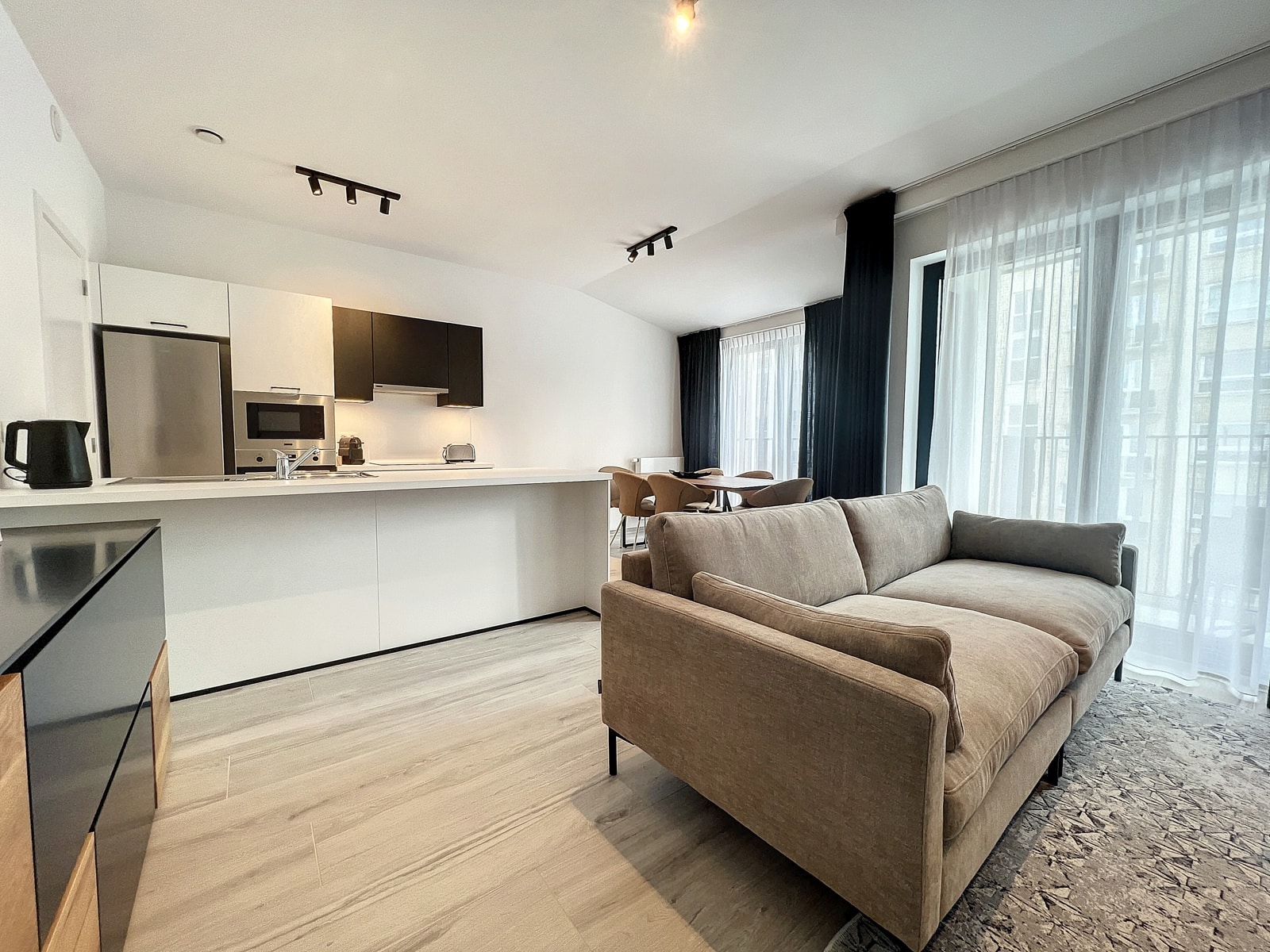 Lichte woonkamer met open keuken - You Real Estate Agency Modern appartement met open keuken, lichte woonkamer en moderne eethoek.