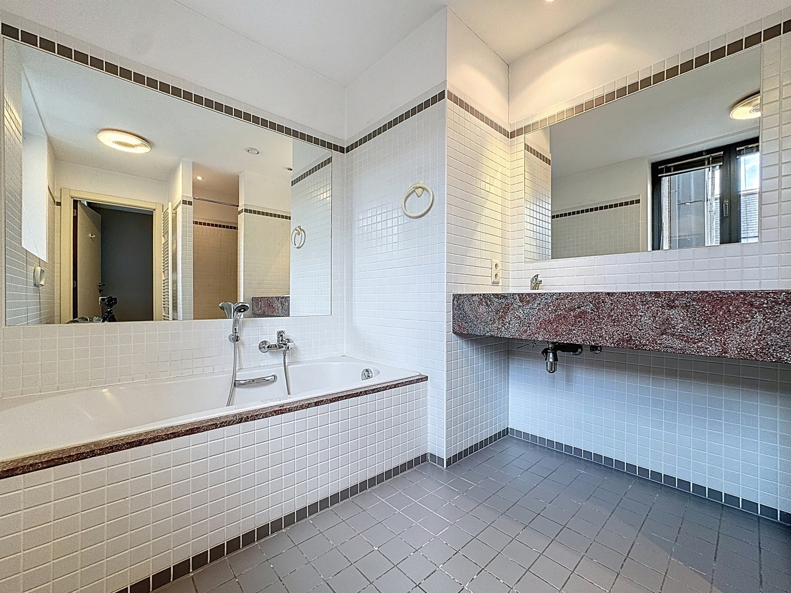 Betegelde badkamer met bad – You Real Estate Agency Een betegelde badkamer met bad en wastafelmeubel in een appartement.