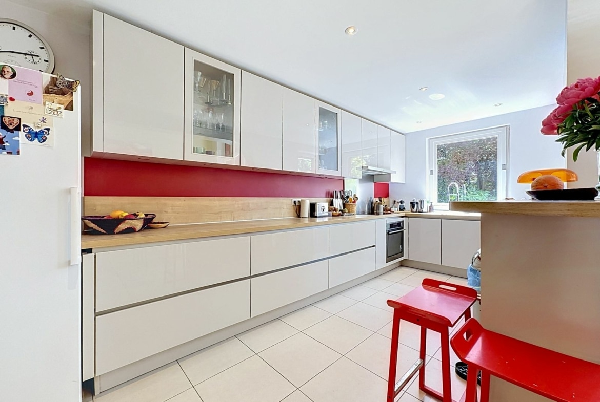 Cuisine moderne blanche avec crédence rouge et îlot, maison lumineuse.