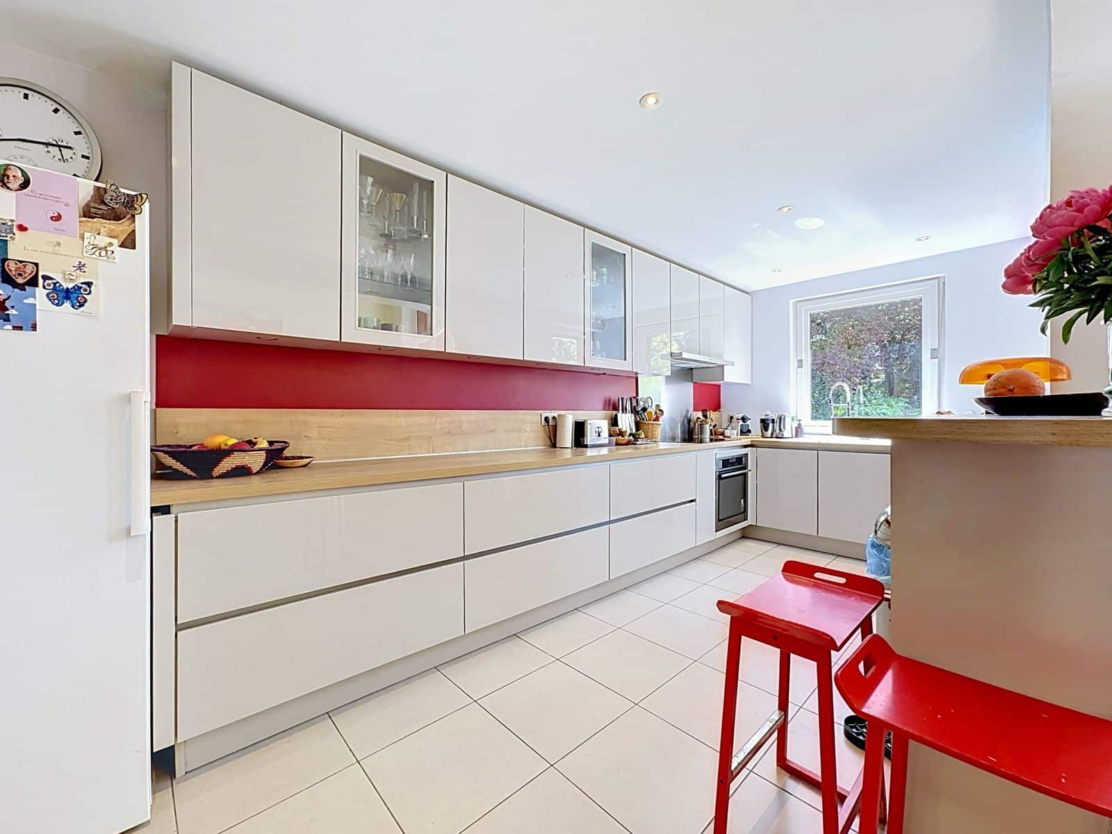 Cuisine Moderne à Crédence Rouge – You Real Estate Agency Cuisine moderne blanche avec crédence rouge et îlot, maison lumineuse.