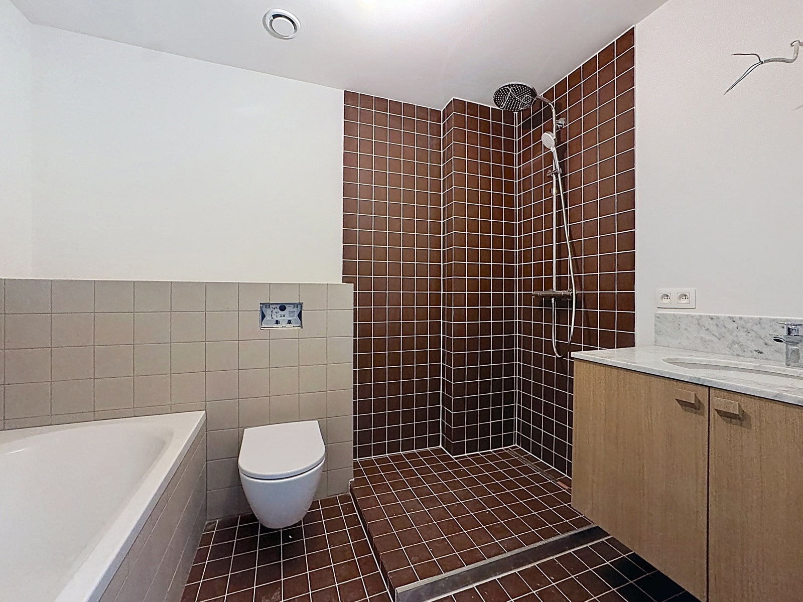 whise photo 23 Bathroom with brown tiled shower area, rainfall shower head, white toilet, and a bathtub to the left behind beige wall tiles, plus a wooden vanity with marble countertop on the right.