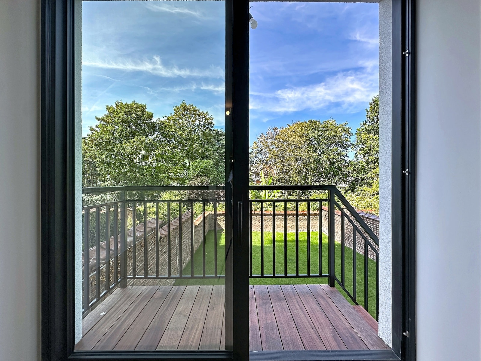 Balcon Avec Vue Sur Jardin Arboré – You Real Estate Agency Appartement lumineux avec terrasse donnant sur jardin arboré et ciel bleu.