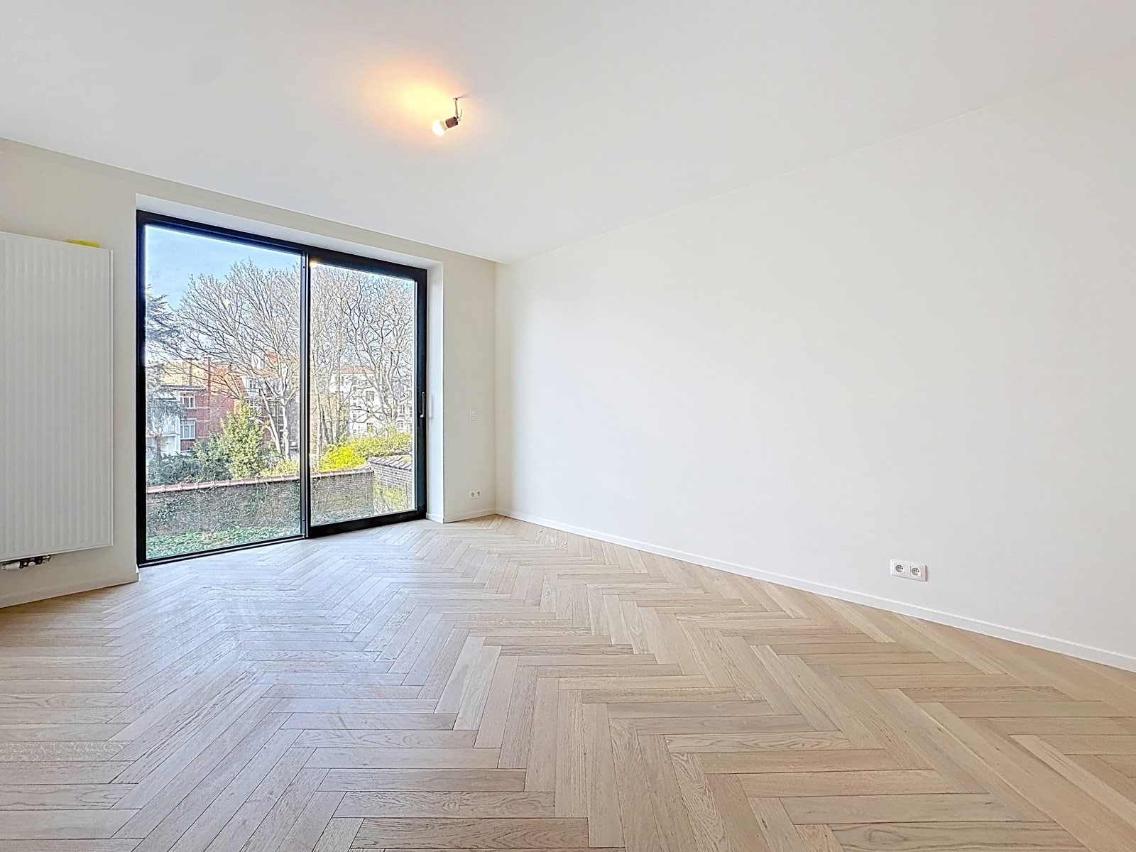 whise photo 9 Bright, empty room with light wood herringbone flooring, white walls, and a large sliding glass door opening to an outdoors view.