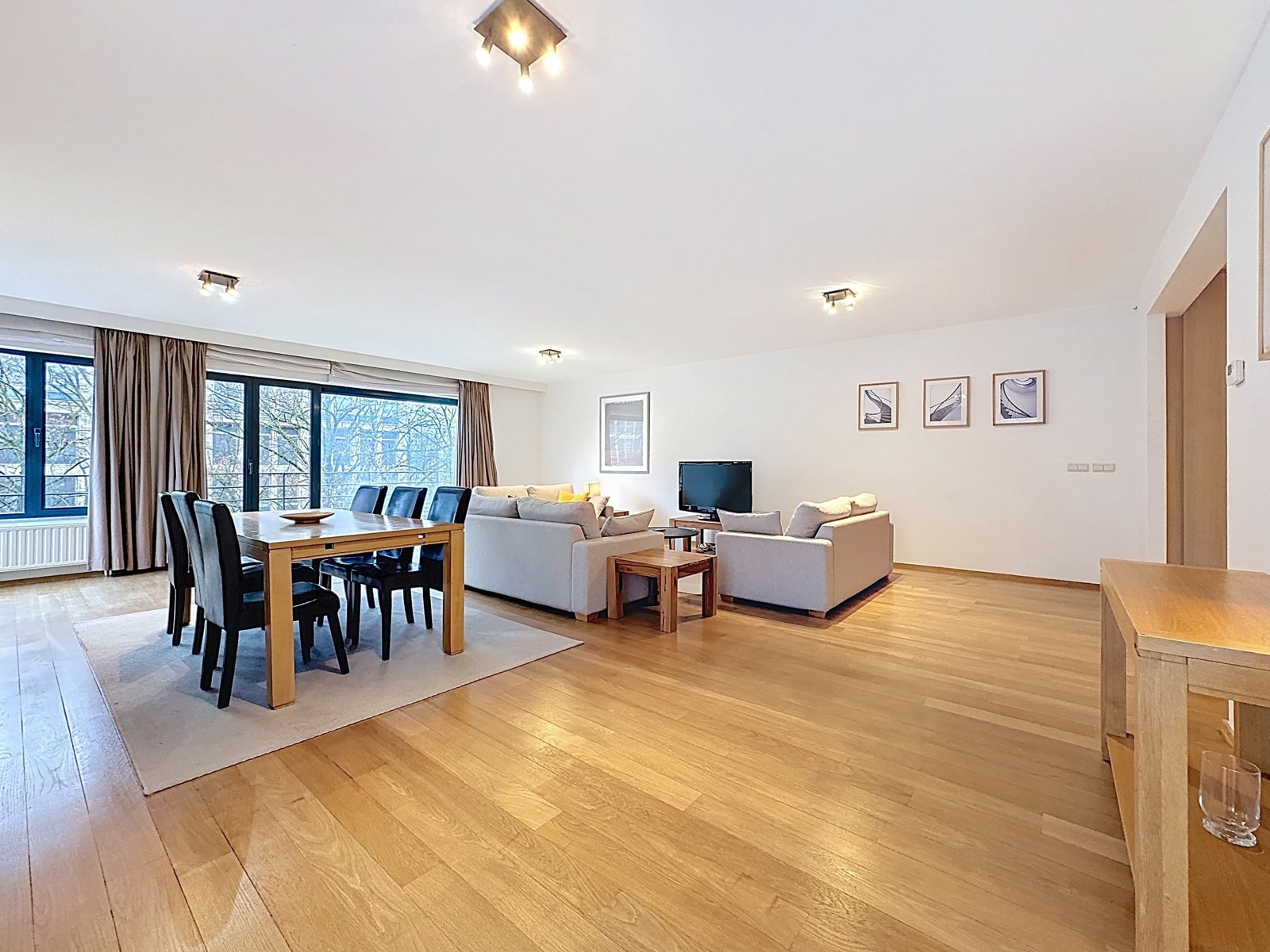 Salon-Salle à Manger Lumineux – You Real Estate Agency Grand salon-salle à manger lumineux avec parquet dans un appartement moderne.
