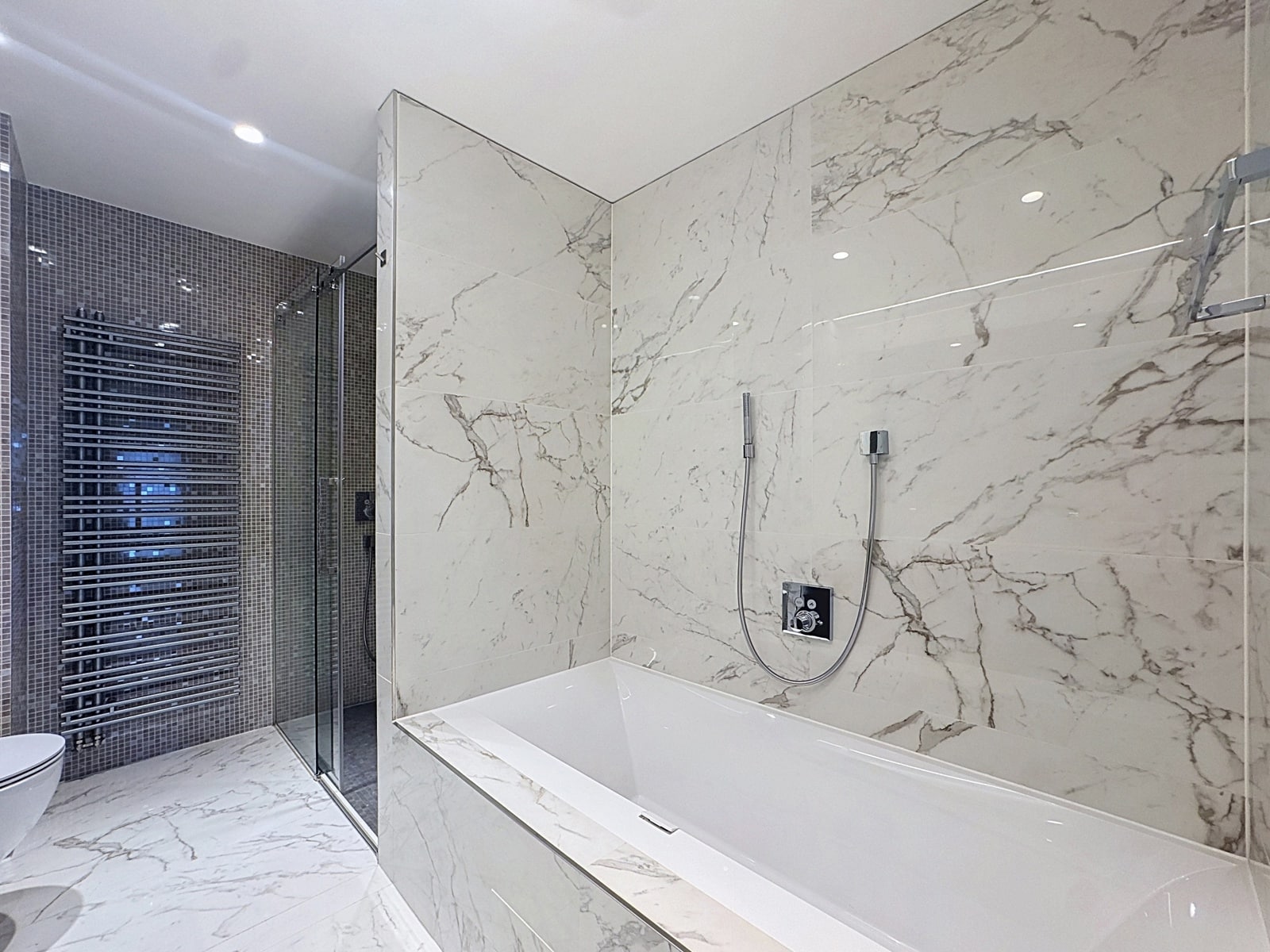 Luxurious Marble Bathroom – You Real Estate Agency Luxurious marble bathroom with a bathtub and glass-enclosed shower in a modern apartment.
