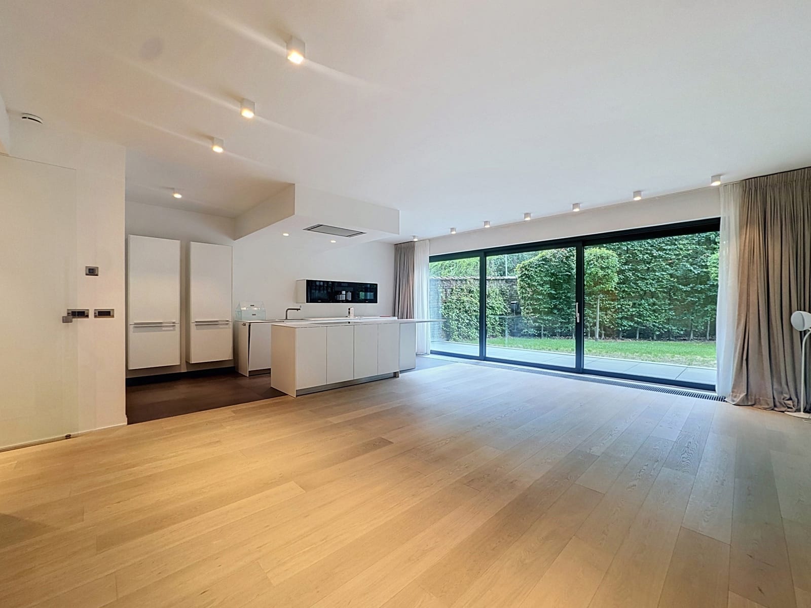 Bright living room with open kitchen - You Real Estate Agency Modern apartment with a bright living room, an open kitchen, and a floor-to-ceiling window overlooking the garden.