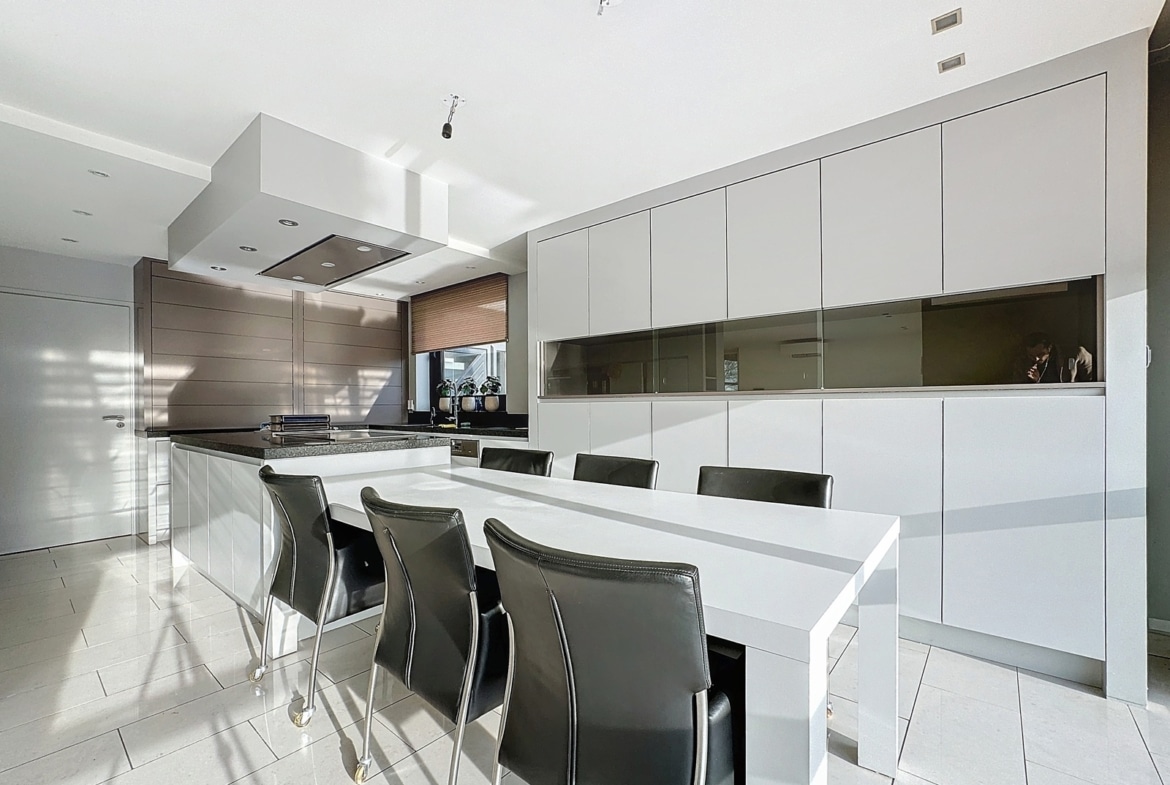 A bright, minimalist kitchen with white cabinets, an island, and a white dining table with black chairs nearby.