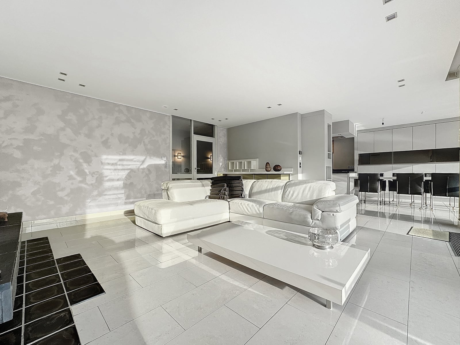 whise photo 6 A bright, modern open-plan living area with a white sectional sofa, polished tile floors, and an adjacent kitchen/dining area.