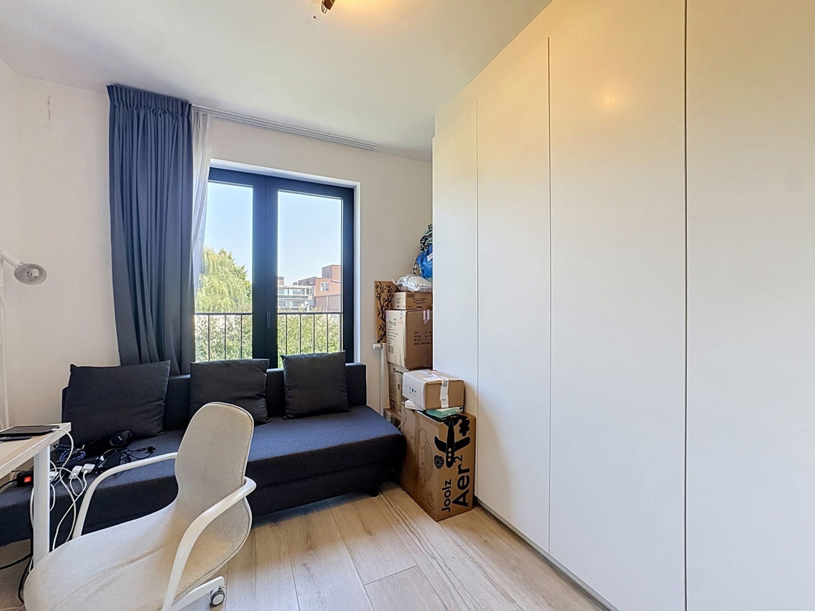 Bureau Lumineux avec Balcon – You Real Estate Agency Pièce polyvalente lumineuse avec canapé, bureau, rangements et balcon en appartement.